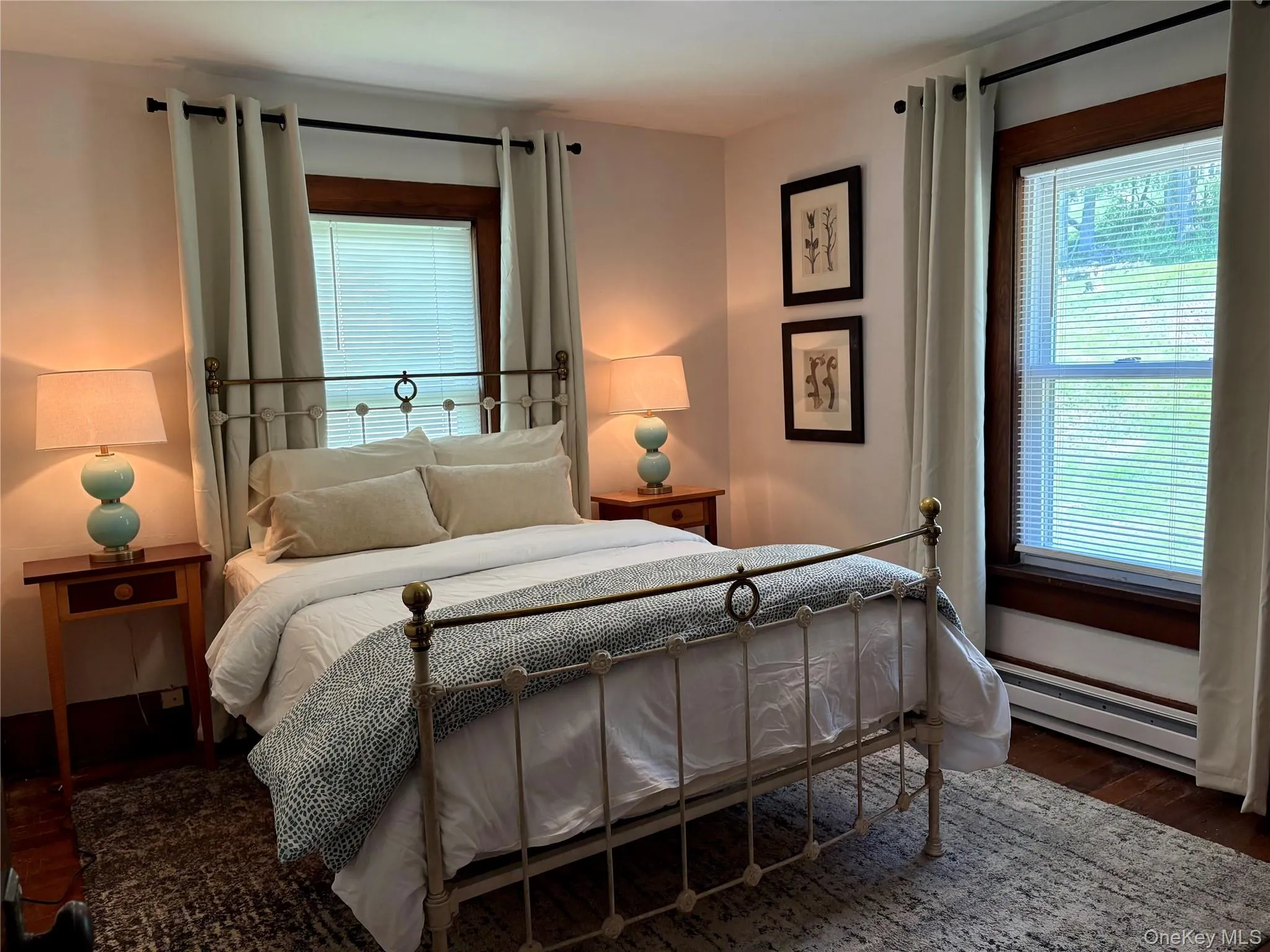 Bedroom featuring a decorative metal bed frame, dark wood-finish flooring, and two windows with wood trim Bedroom featuring a decorative metal bed frame, dark wood-finish flooring, and two windows with wood trim