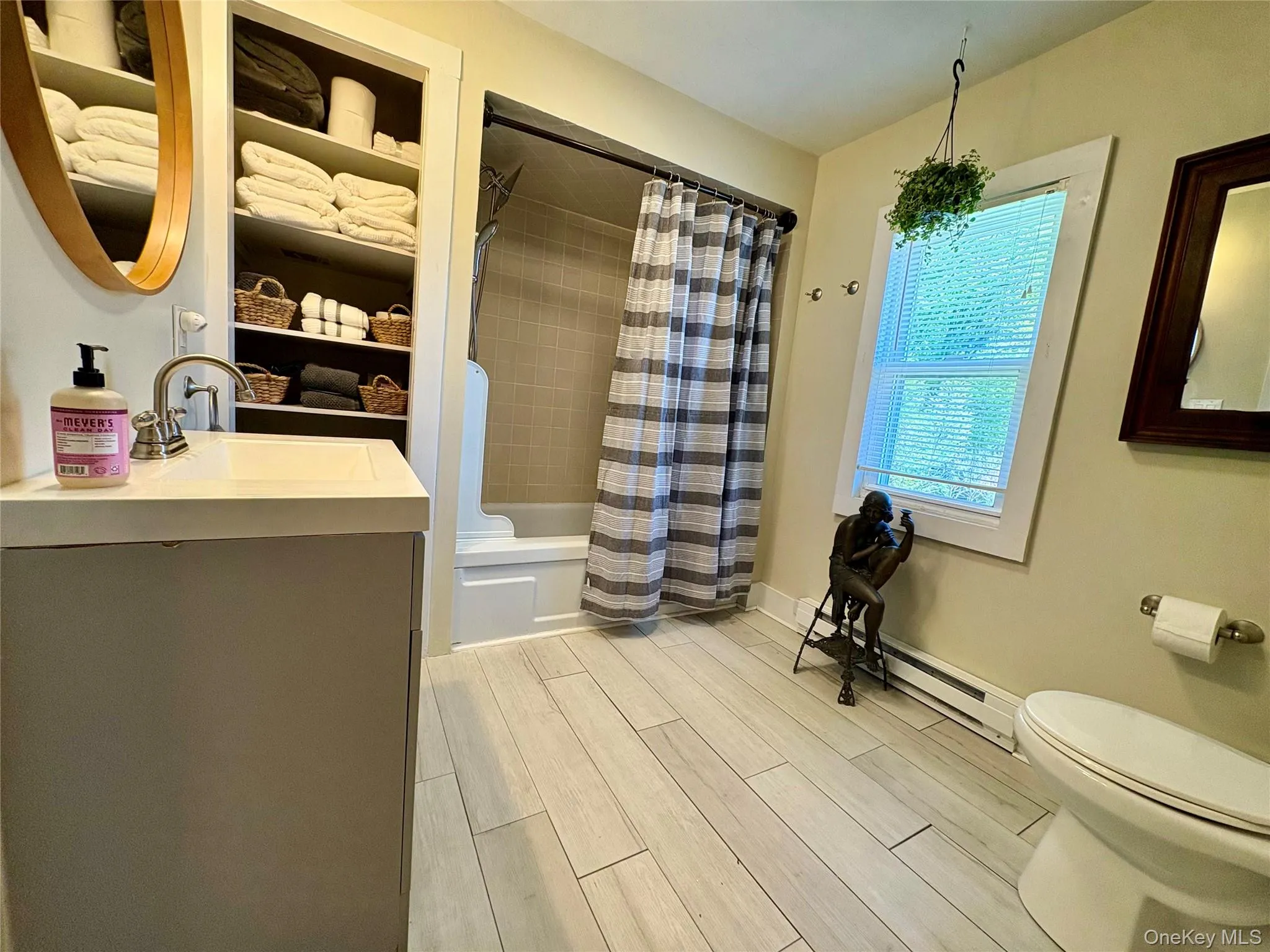 Bathroom featuring a single vanity with an integrated sink, built-in shelving, a full-size window with blinds, and light wood-finish plank flooring Bathroom featuring a single vanity with an integrated sink, built-in shelving, a full-size window with blinds, and light wood-finish plank flooring