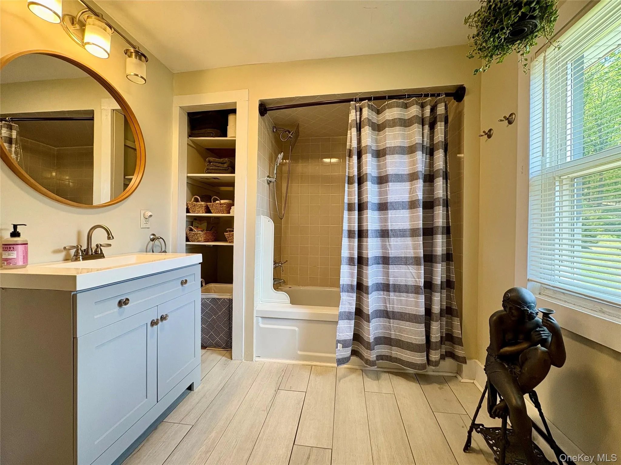 Bathroom featuring a light blue vanity with a white countertop and brushed nickel hardware, a wood-frame round mirror, and a three-bulb light fixture Bathroom featuring a light blue vanity with a white countertop and brushed nickel hardware, a wood-frame round mirror, and a three-bulb light fixture