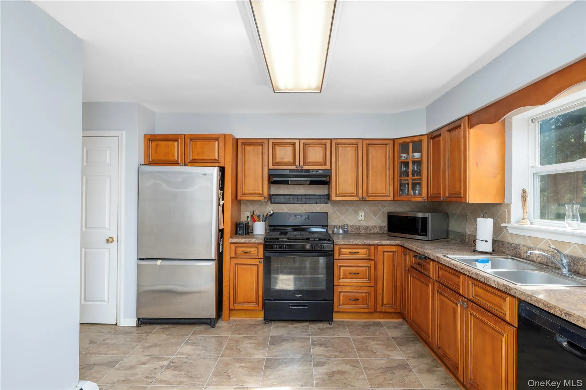 Kitchen featuring wood cabinetry, stainless steel appliances, tiled flooring, and a window above the sink Kitchen featuring wood cabinetry, stainless steel appliances, tiled flooring, and a window above the sink