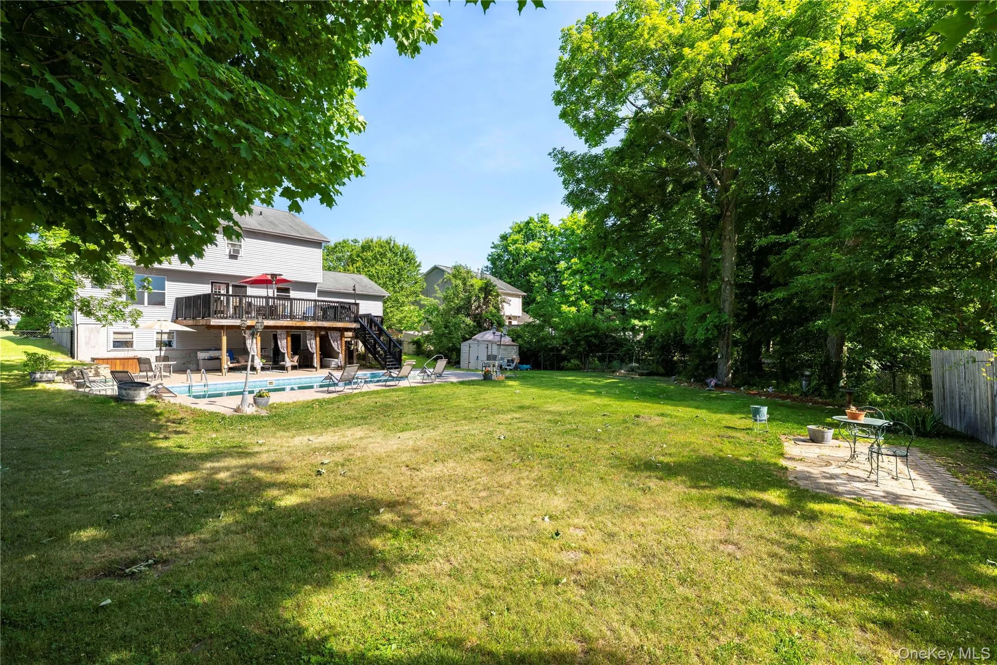 Expansive backyard featuring a large in-ground swimming pool, a two-story deck with a covered lower level, mature trees, and a spacious lawn area Expansive backyard featuring a large in-ground swimming pool, a two-story deck with a covered lower level, mature trees, and a spacious lawn area