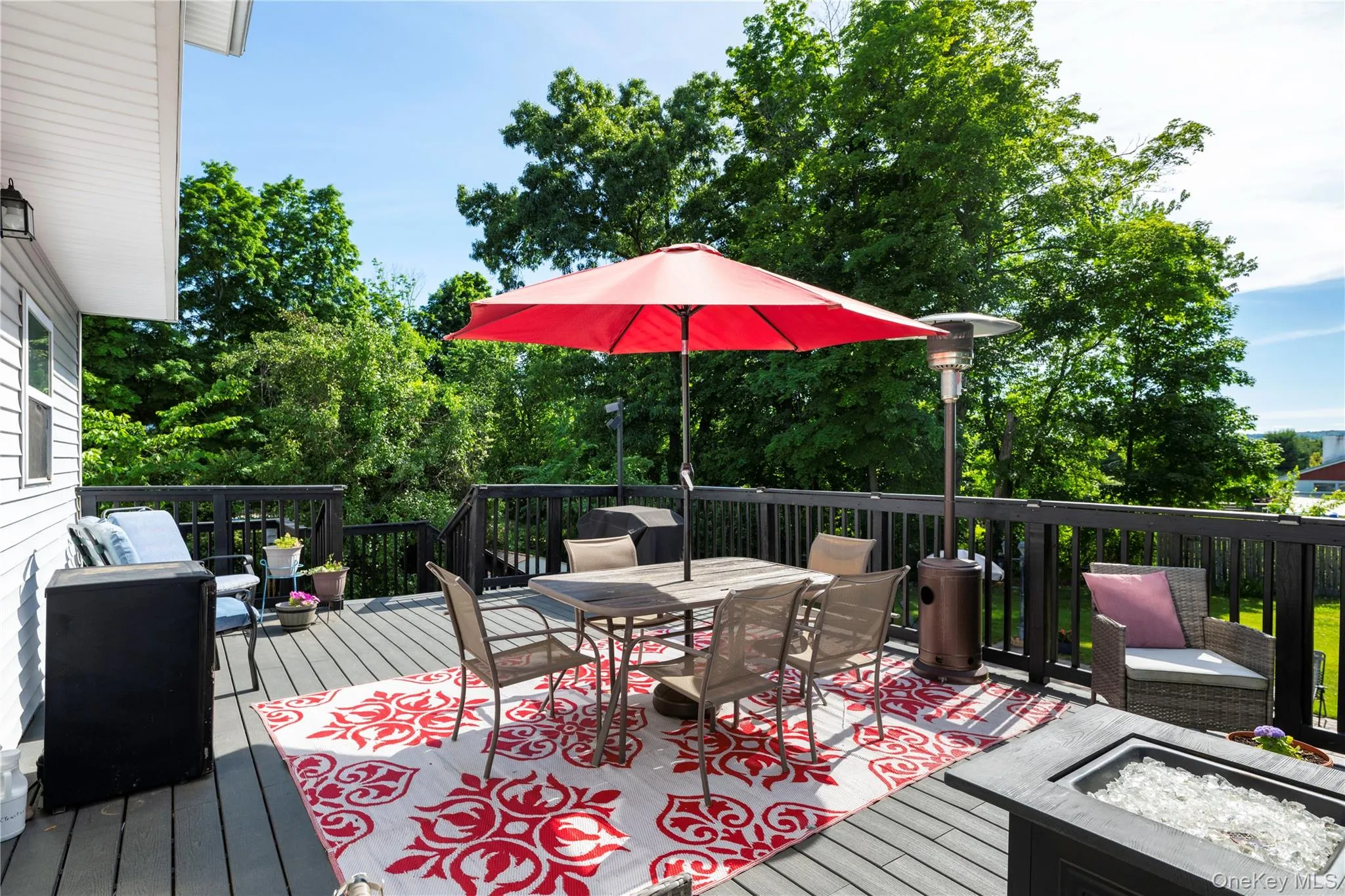 Spacious elevated deck featuring a fire pit, dark wood railing, and an exterior wall lantern Spacious elevated deck featuring a fire pit, dark wood railing, and an exterior wall lantern