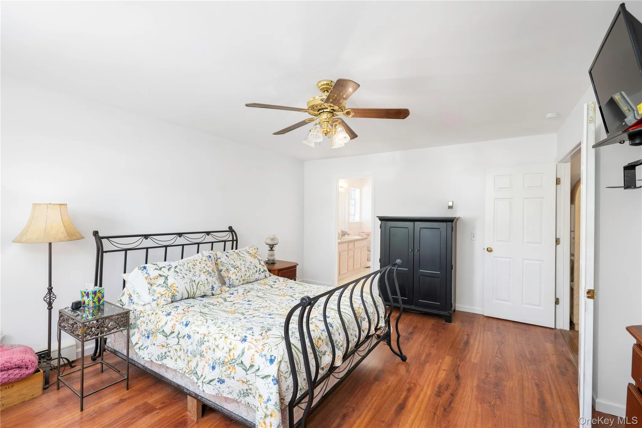 Spacious room featuring wood-finish flooring, a ceiling fan with integrated lighting, white walls, and a visible doorway leading to an additional space Spacious room featuring wood-finish flooring, a ceiling fan with integrated lighting, white walls, and a visible doorway leading to an additional space