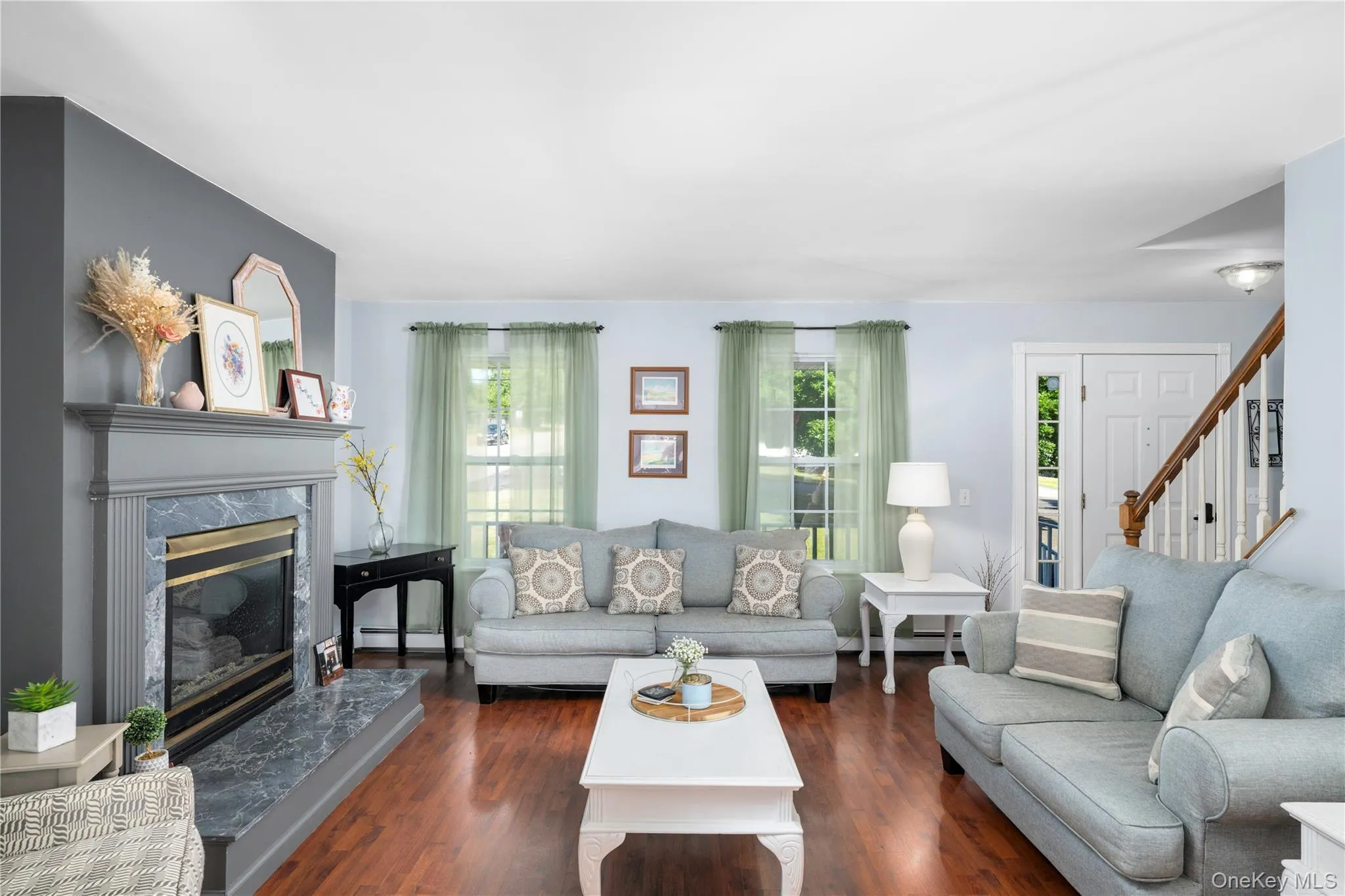 Living room featuring wood-finish flooring and a fireplace with a gray mantle and hearth Living room featuring wood-finish flooring and a fireplace with a gray mantle and hearth