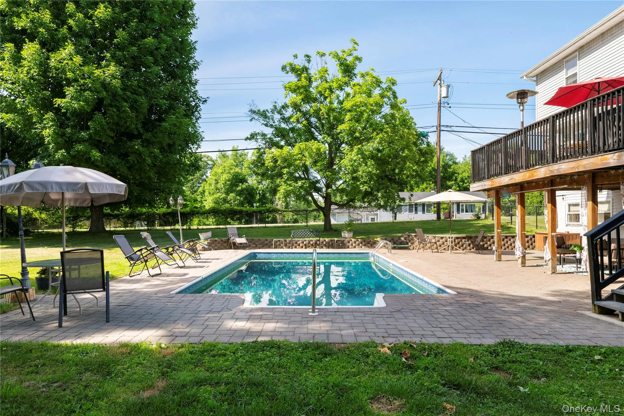 In-ground swimming pool with a brick paver surround, expansive wood deck, private patio space, and mature trees In-ground swimming pool with a brick paver surround, expansive wood deck, private patio space, and mature trees