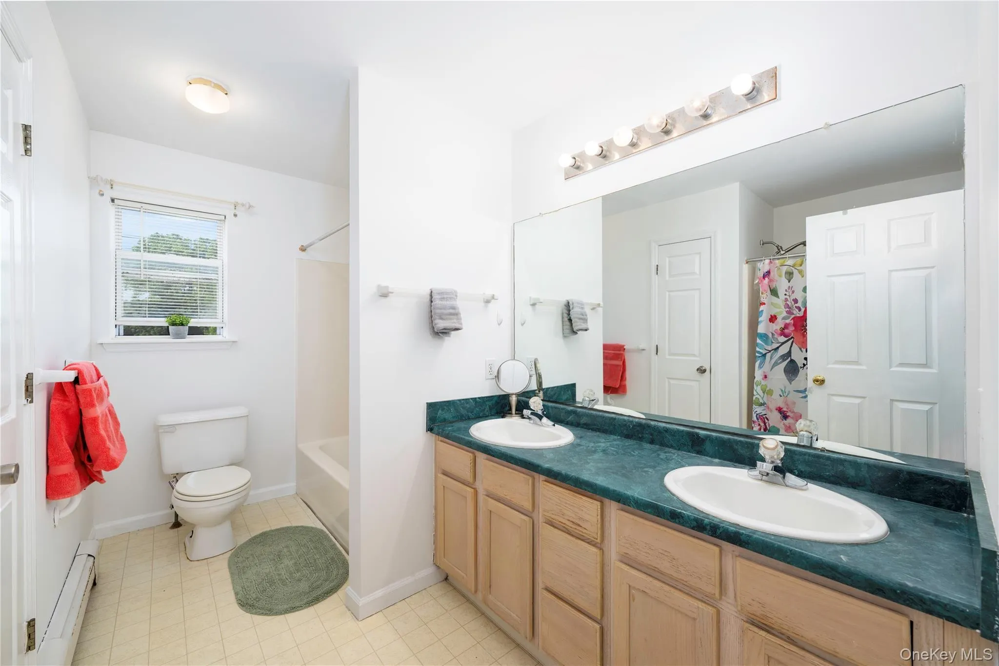Bathroom featuring a dual vanity with a green countertop, light wood-finish cabinetry, and a full-width mirror Bathroom featuring a dual vanity with a green countertop, light wood-finish cabinetry, and a full-width mirror
