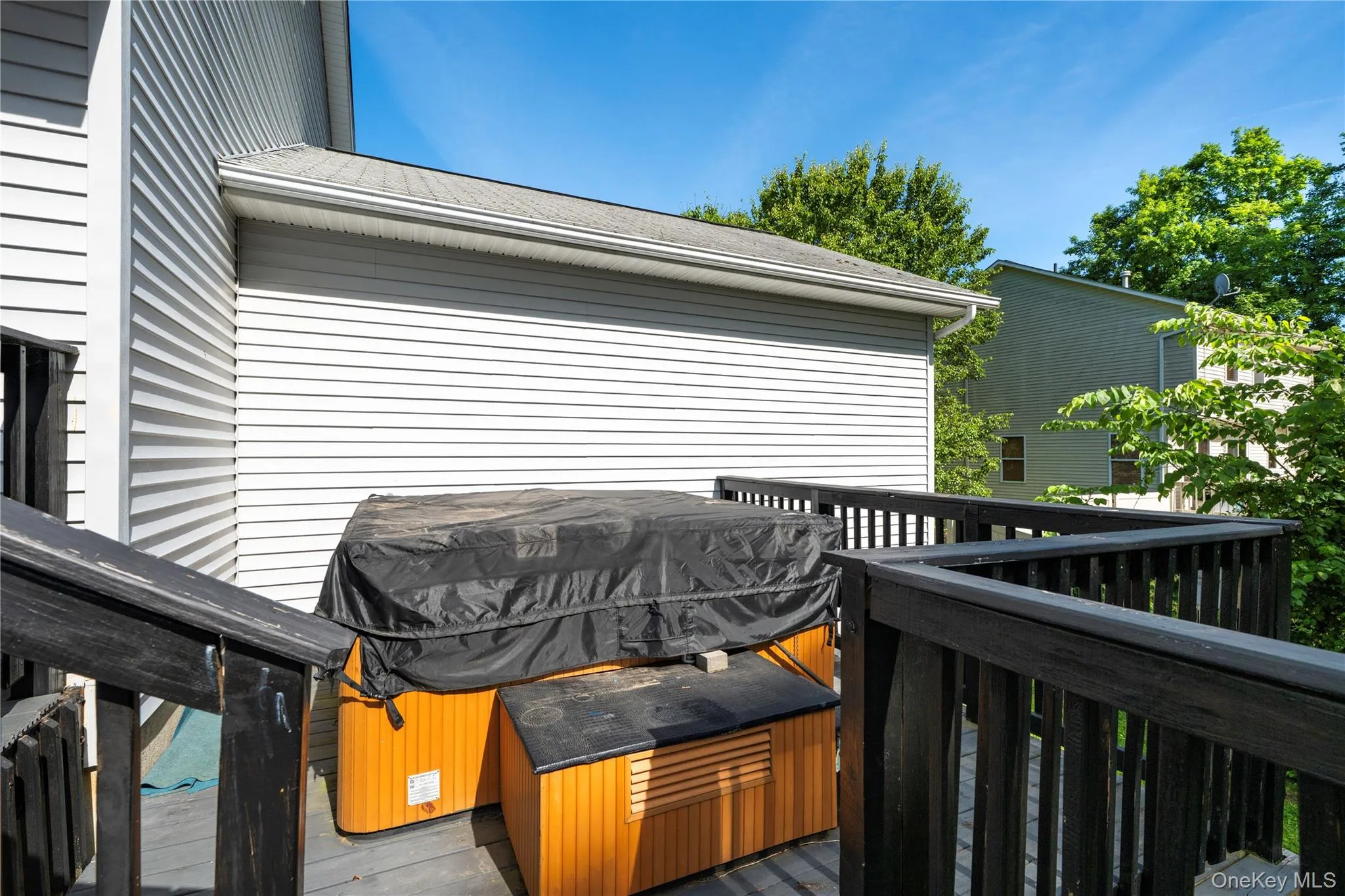 Outdoor deck space featuring a built-in hot tub, dark wood railing, and white horizontal siding Outdoor deck space featuring a built-in hot tub, dark wood railing, and white horizontal siding