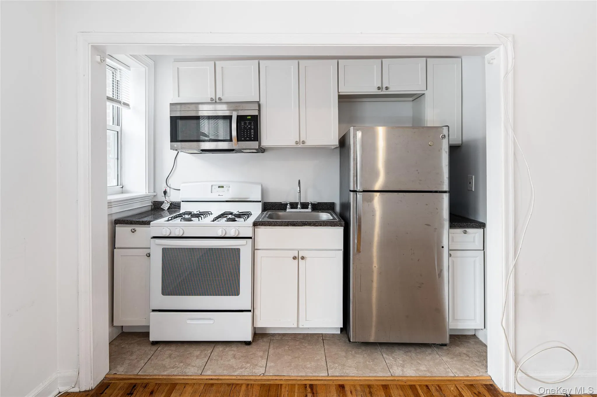 Kitchen featuring stainless steel appliances, dark countertops, light wood-type flooring, and white cabinets Kitchen featuring stainless steel appliances, dark countertops, light wood-type flooring, and white cabinets