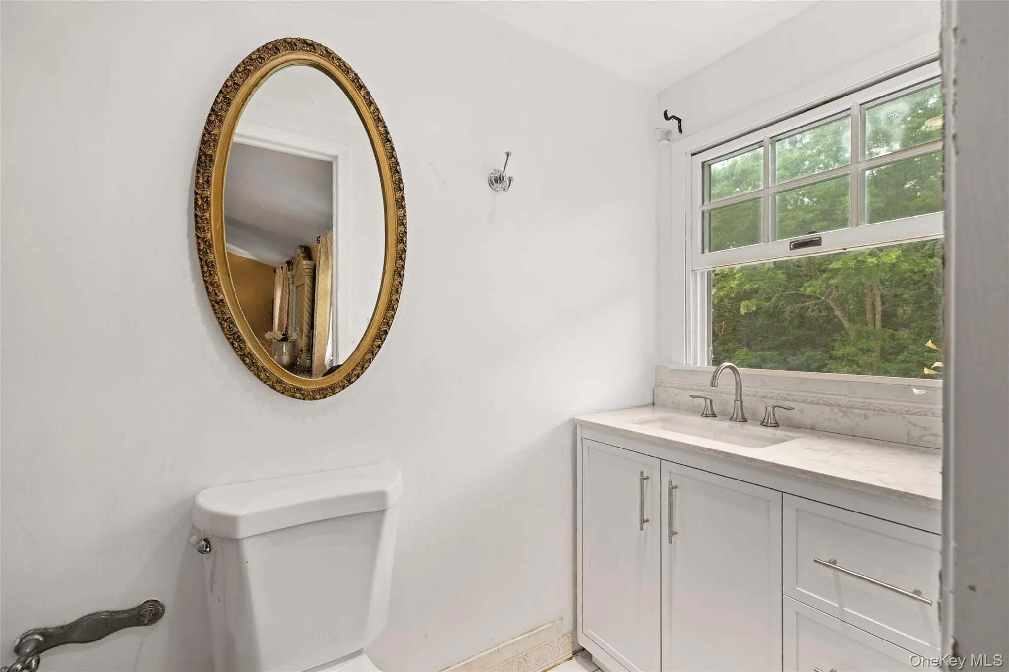 Bathroom featuring a white vanity with integrated sink, brushed nickel faucet, and a large window with exterior foliage Bathroom featuring a white vanity with integrated sink, brushed nickel faucet, and a large window with exterior foliage