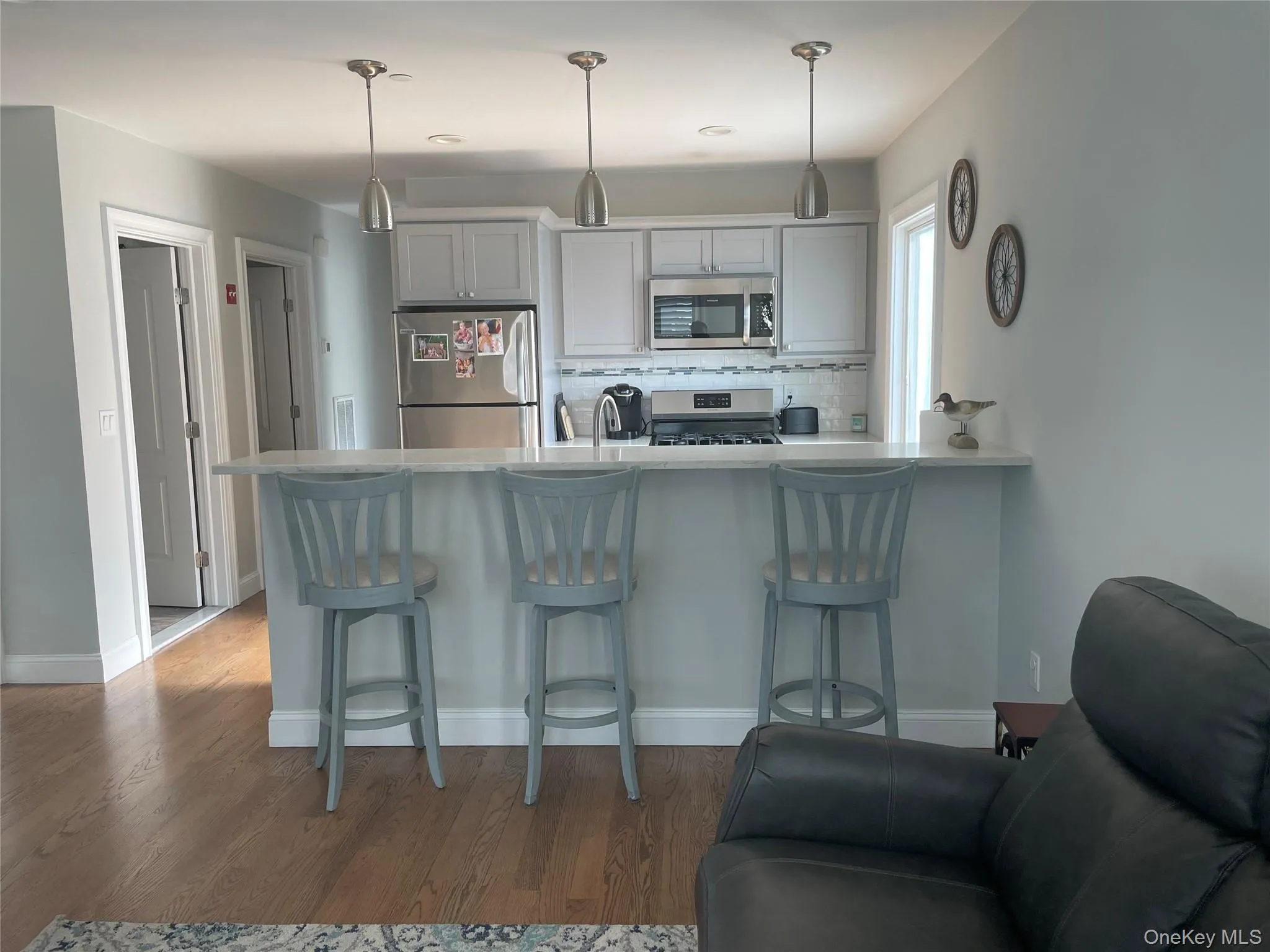 Kitchen featuring appliances with stainless steel finishes, a kitchen breakfast bar, tasteful backsplash, light countertops, and wood finished floors Kitchen featuring appliances with stainless steel finishes, a kitchen breakfast bar, tasteful backsplash, light countertops, and wood finished floors