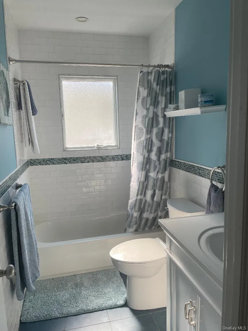 Full bathroom with shower / bath combination with curtain, tile patterned floors, vanity, tile walls, and wainscoting Full bathroom with shower / bath combination with curtain, tile patterned floors, vanity, tile walls, and wainscoting