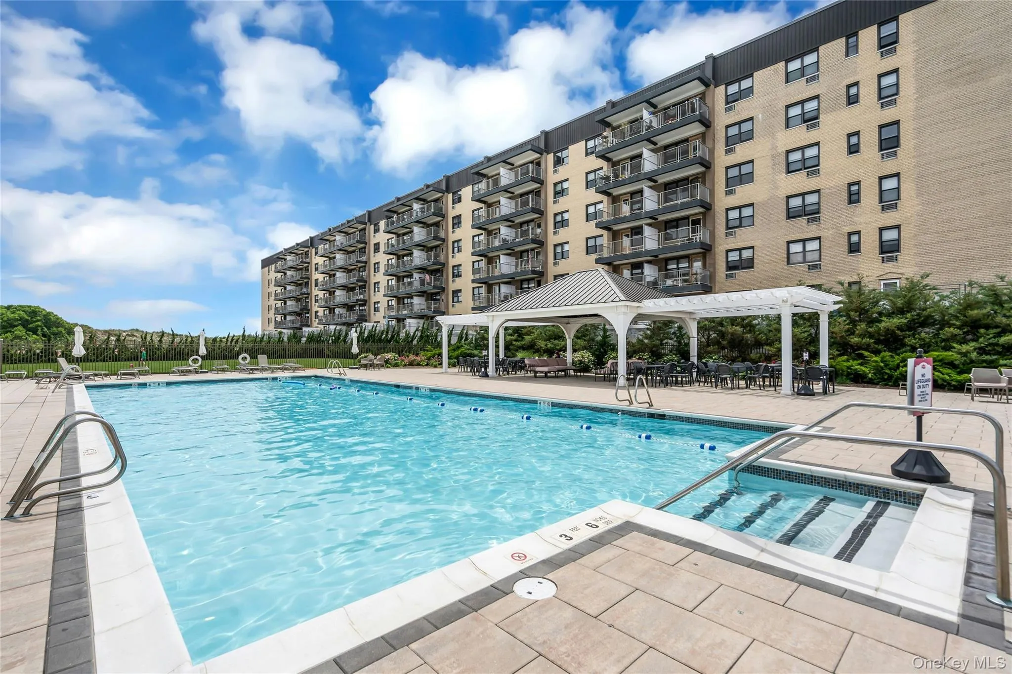 Expansive outdoor pool area featuring a large swimming pool, and a surrounding paver patio Expansive outdoor pool area featuring a large swimming pool, and a surrounding paver patio