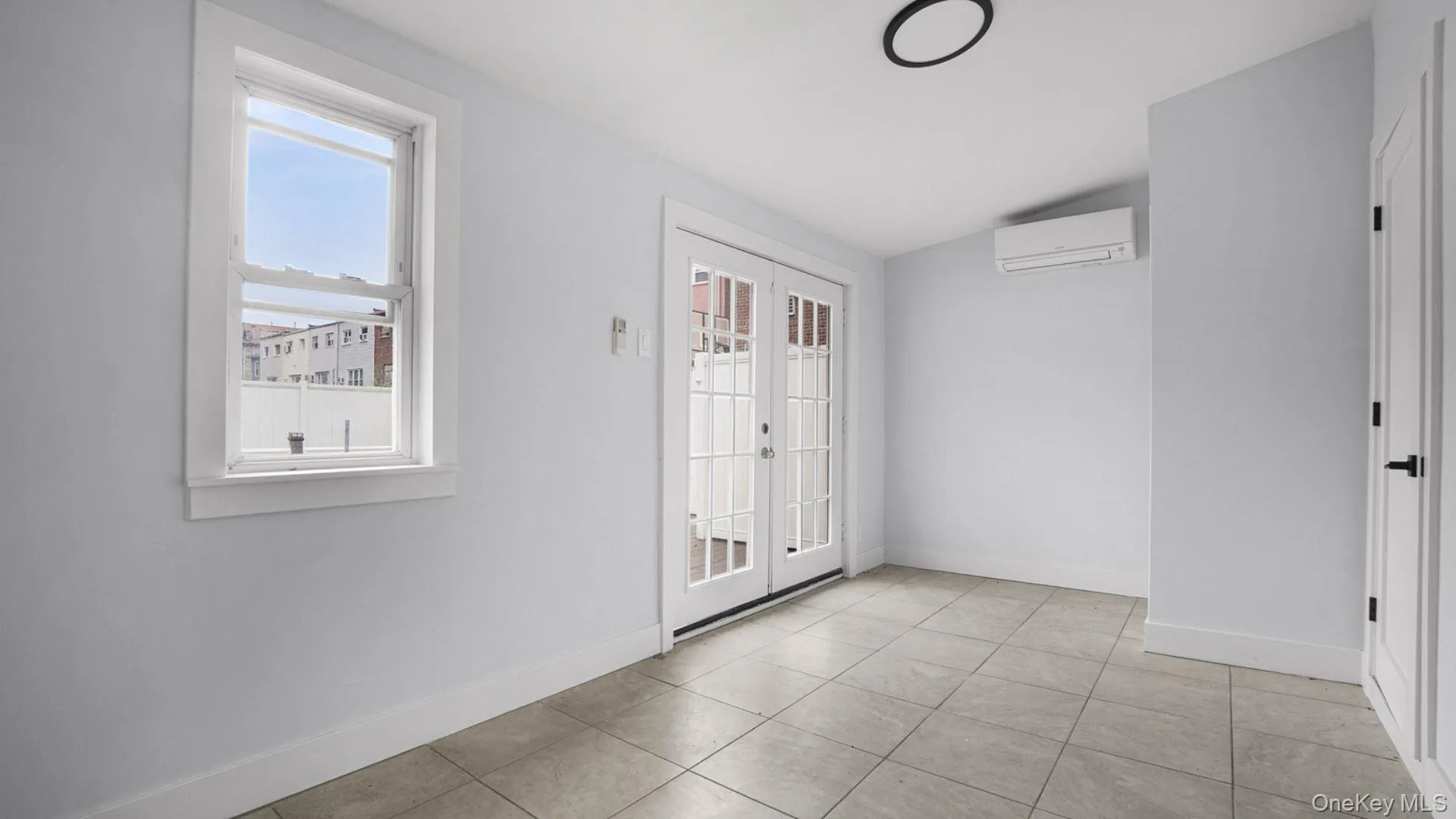 Empty room featuring light tile patterned flooring, a wall mounted air conditioner, french doors, and vaulted ceiling Empty room featuring light tile patterned flooring, a wall mounted air conditioner, french doors, and vaulted ceiling
