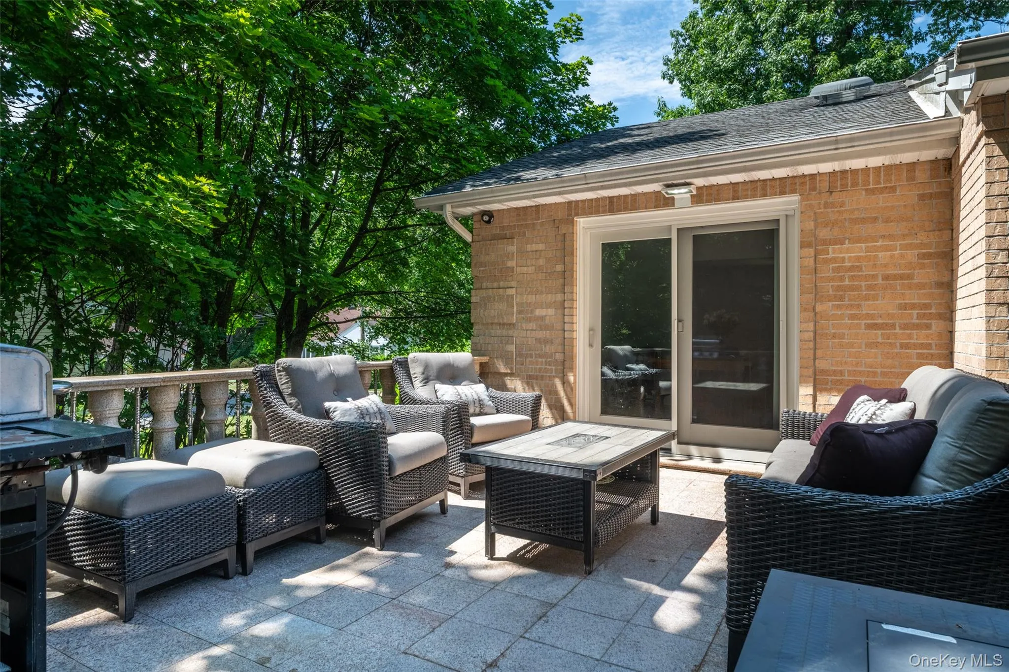 Expansive outdoor patio featuring paver flooring, a brick exterior wall, and a sliding glass door Expansive outdoor patio featuring paver flooring, a brick exterior wall, and a sliding glass door