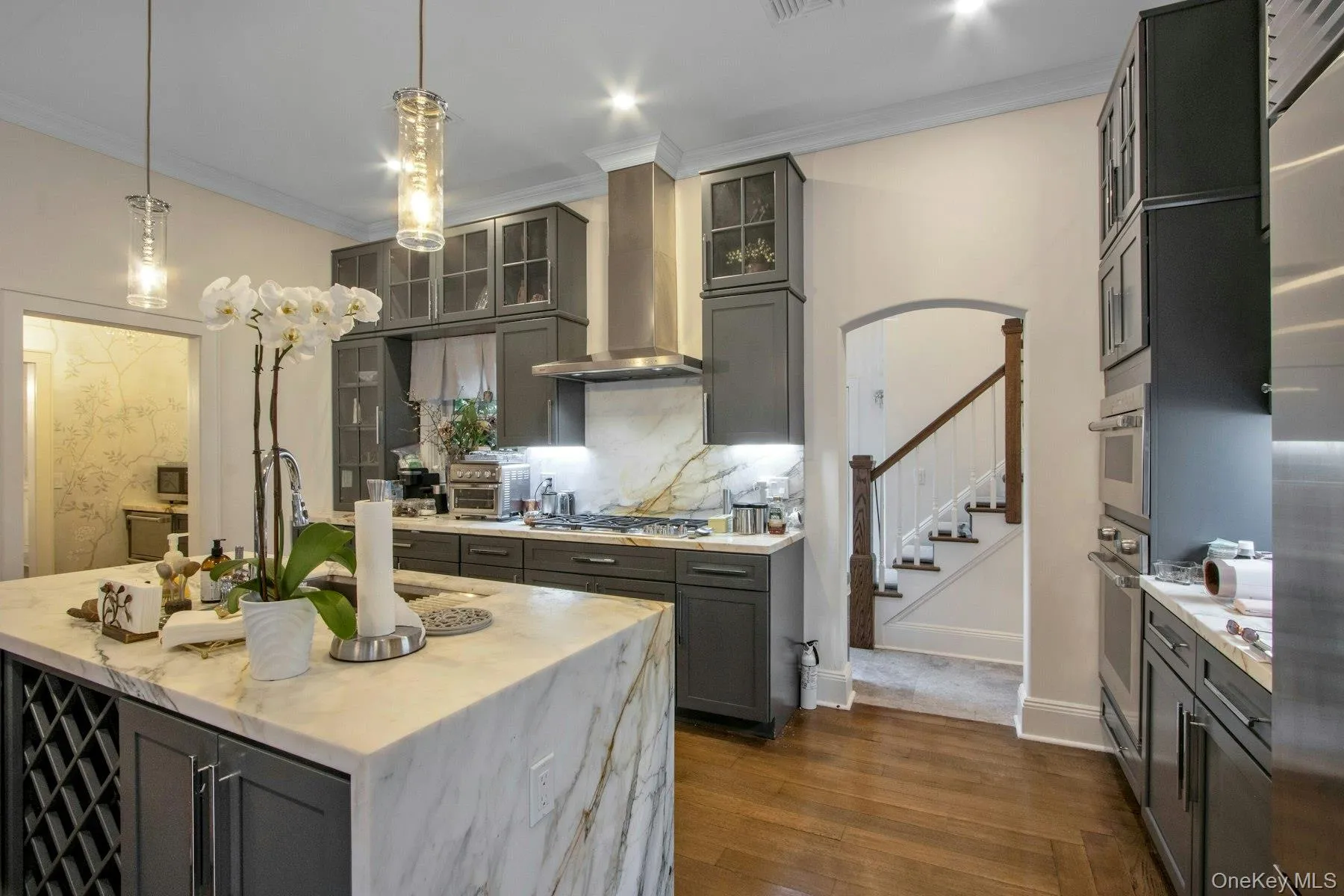 Kitchen with gray cabinetry, wall chimney exhaust hood, dark hardwood / wood-style flooring, an island with sink, and pendant lighting Kitchen with gray cabinetry, wall chimney exhaust hood, dark hardwood / wood-style flooring, an island with sink, and pendant lighting