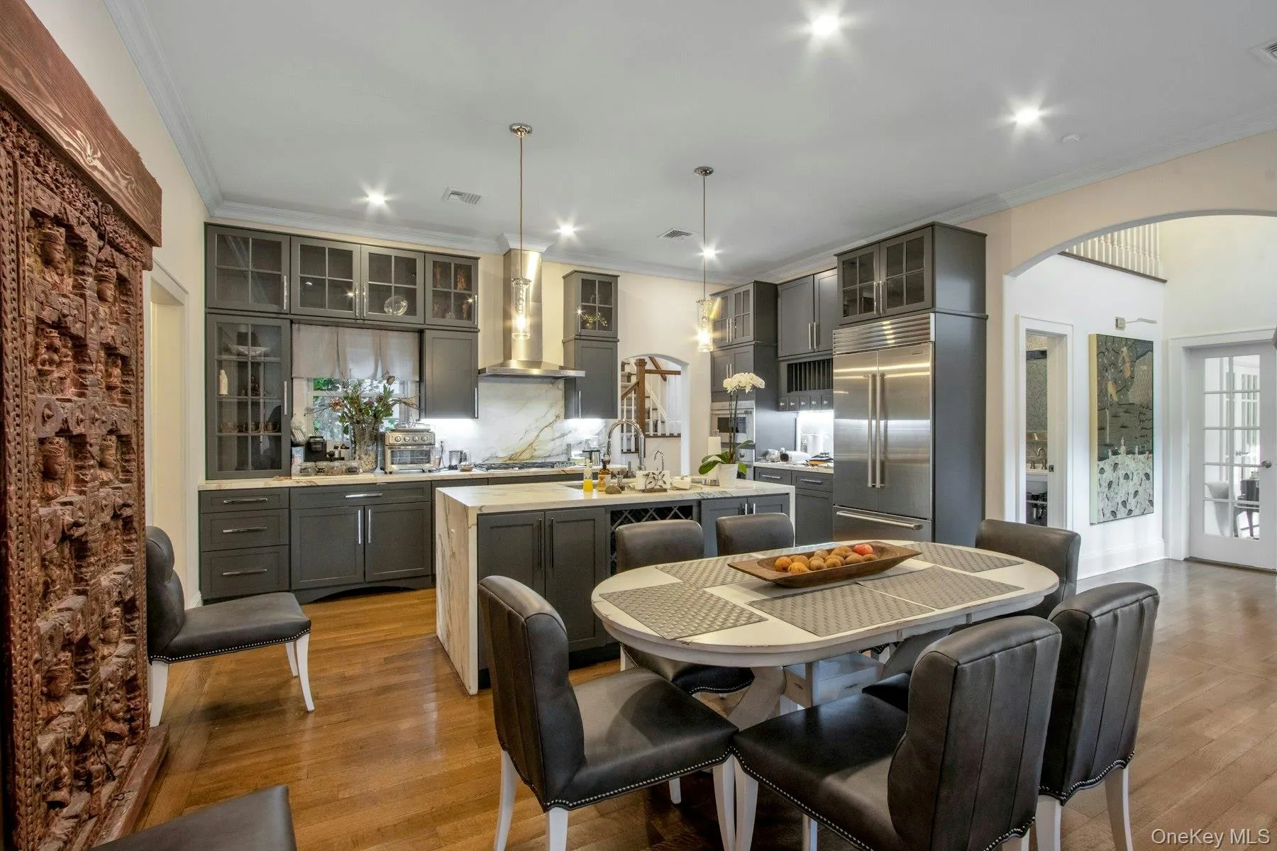 Kitchen with appliances with stainless steel finishes, a kitchen island with sink, wall chimney range hood, pendant lighting, and light hardwood / wood-style flooring Kitchen with appliances with stainless steel finishes, a kitchen island with sink, wall chimney range hood, pendant lighting, and light hardwood / wood-style flooring