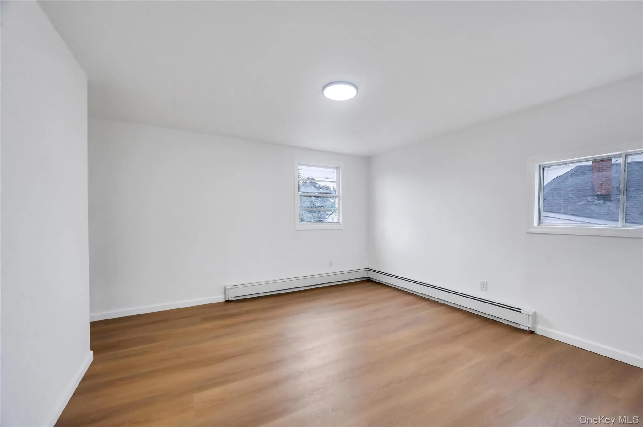 Bright interior space featuring wood-finish flooring, white walls, and a contemporary flush-mount ceiling light Bright interior space featuring wood-finish flooring, white walls, and a contemporary flush-mount ceiling light