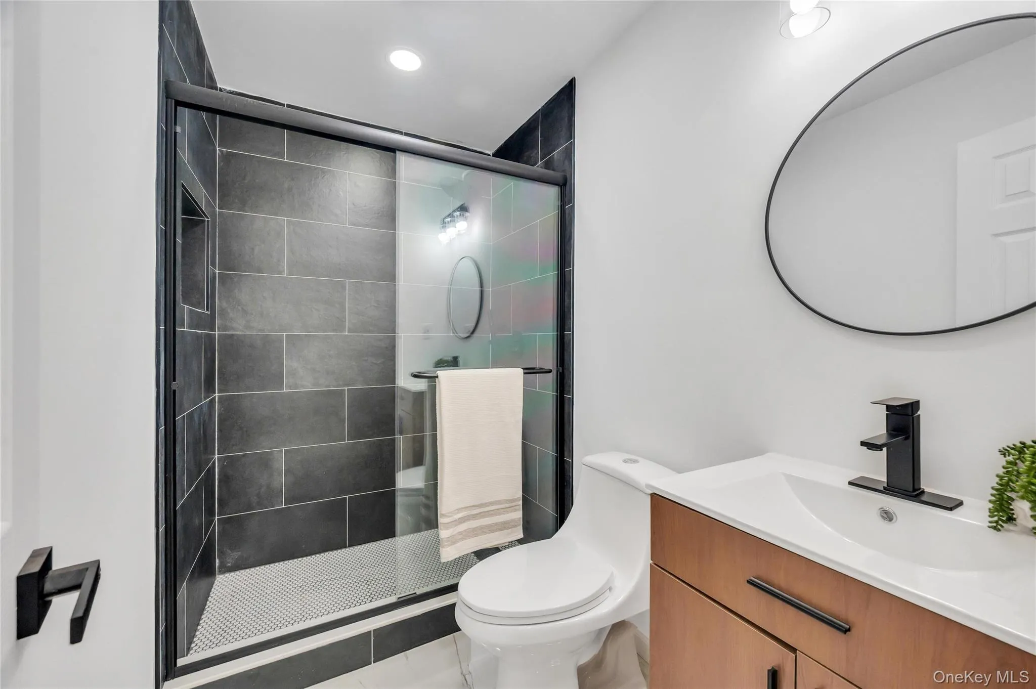 Modern bathroom featuring a walk-in shower with dark grey rectangular tile, a sliding glass door, and a built-in shower niche Modern bathroom featuring a walk-in shower with dark grey rectangular tile, a sliding glass door, and a built-in shower niche