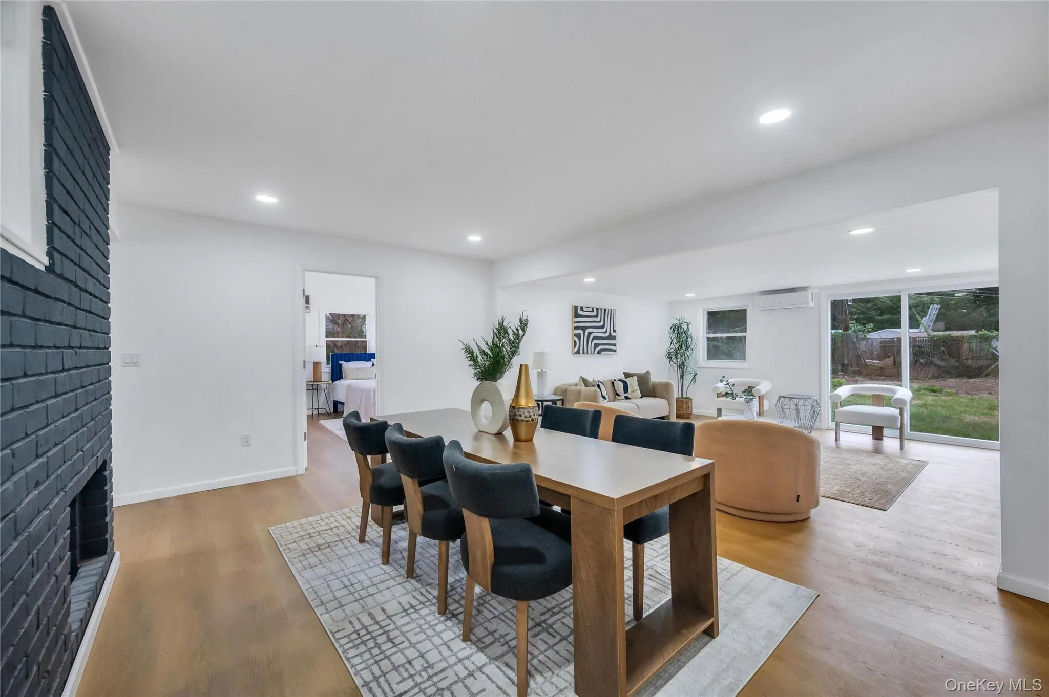 Open-concept living area featuring wood-finish flooring, a painted brick fireplace, recessed lighting, and sliding glass doors to the exterior Open-concept living area featuring wood-finish flooring, a painted brick fireplace, recessed lighting, and sliding glass doors to the exterior