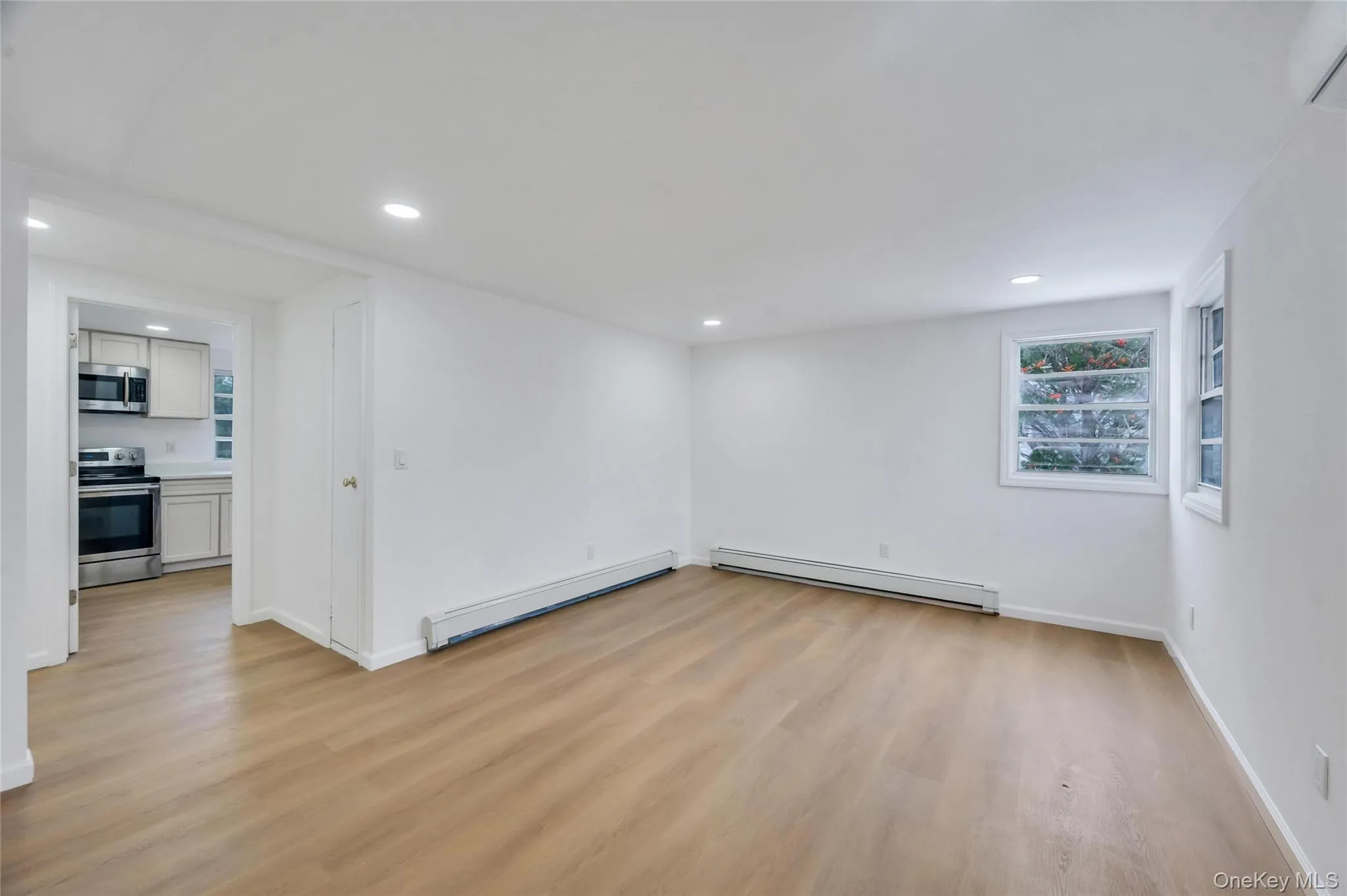 Spacious room with wood-finish flooring, recessed lighting, and white walls Spacious room with wood-finish flooring, recessed lighting, and white walls