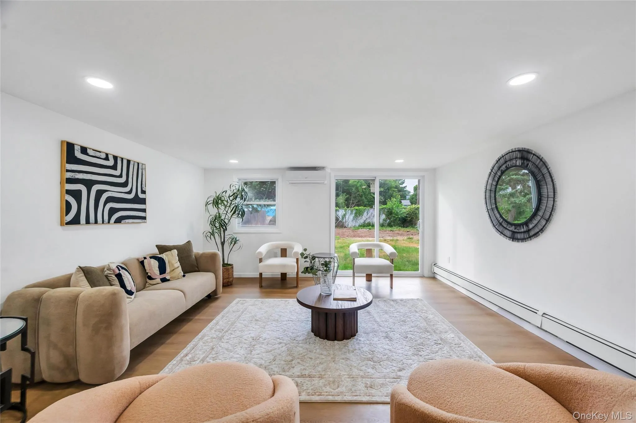 Spacious living area featuring wood-finish flooring, recessed lighting, and a sliding glass door providing direct outdoor access Spacious living area featuring wood-finish flooring, recessed lighting, and a sliding glass door providing direct outdoor access