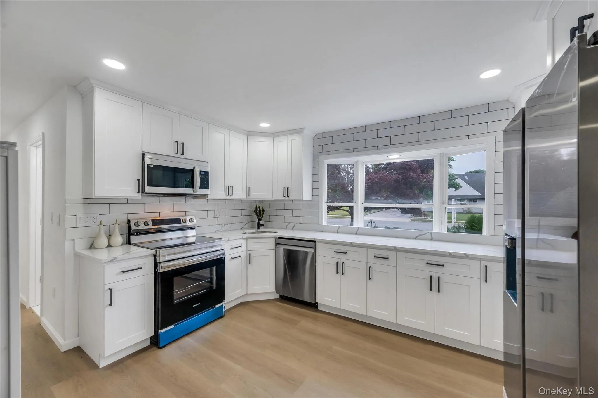 Contemporary kitchen featuring white shaker cabinetry, stainless steel appliances, marble-look countertops, subway tile backsplash, and light wood-finish flooring Contemporary kitchen featuring white shaker cabinetry, stainless steel appliances, marble-look countertops, subway tile backsplash, and light wood-finish flooring