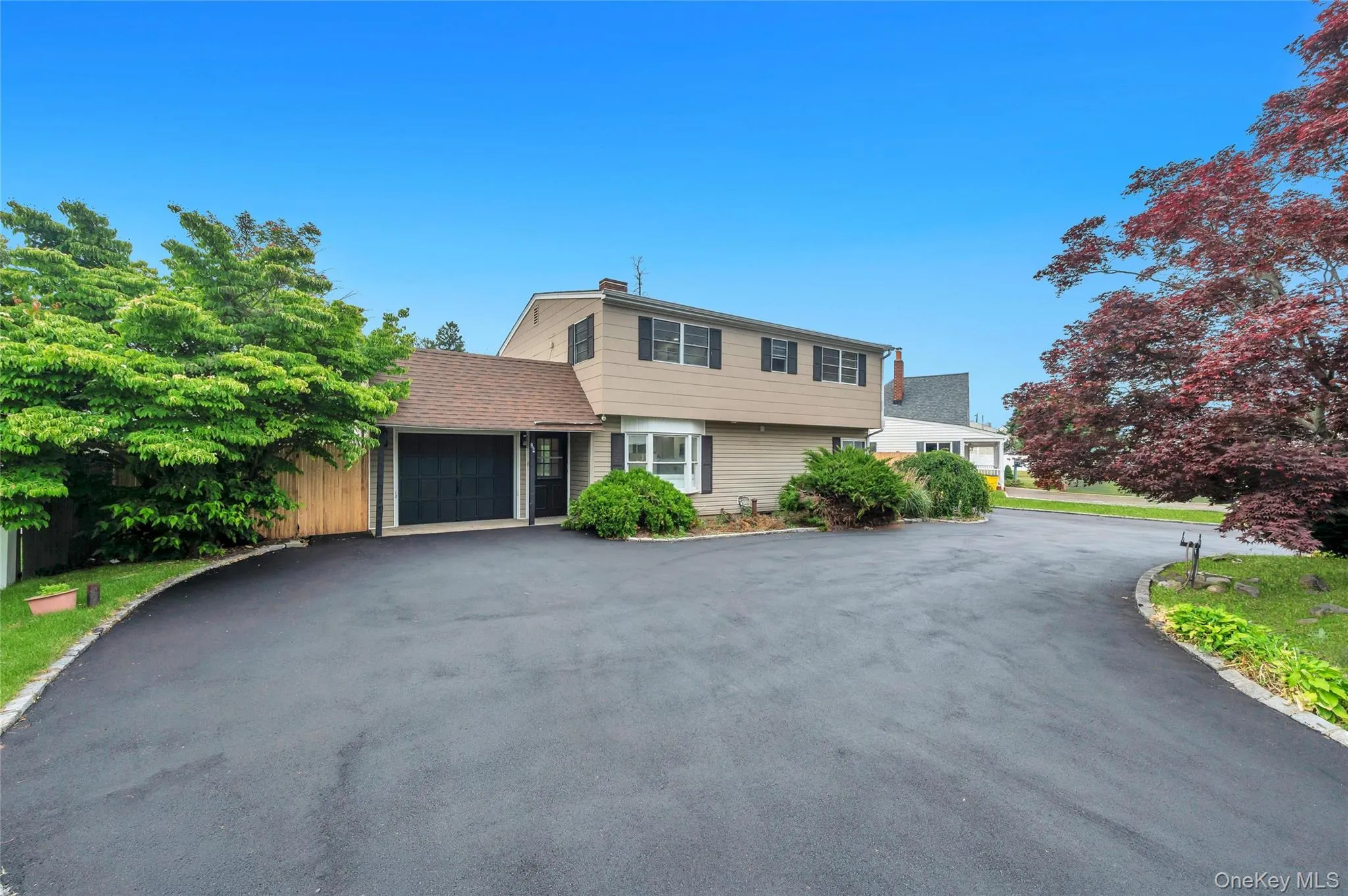 Split-level residence featuring a tan exterior with dark shutters, a front-facing garage with a dark door, and a bay window Split-level residence featuring a tan exterior with dark shutters, a front-facing garage with a dark door, and a bay window