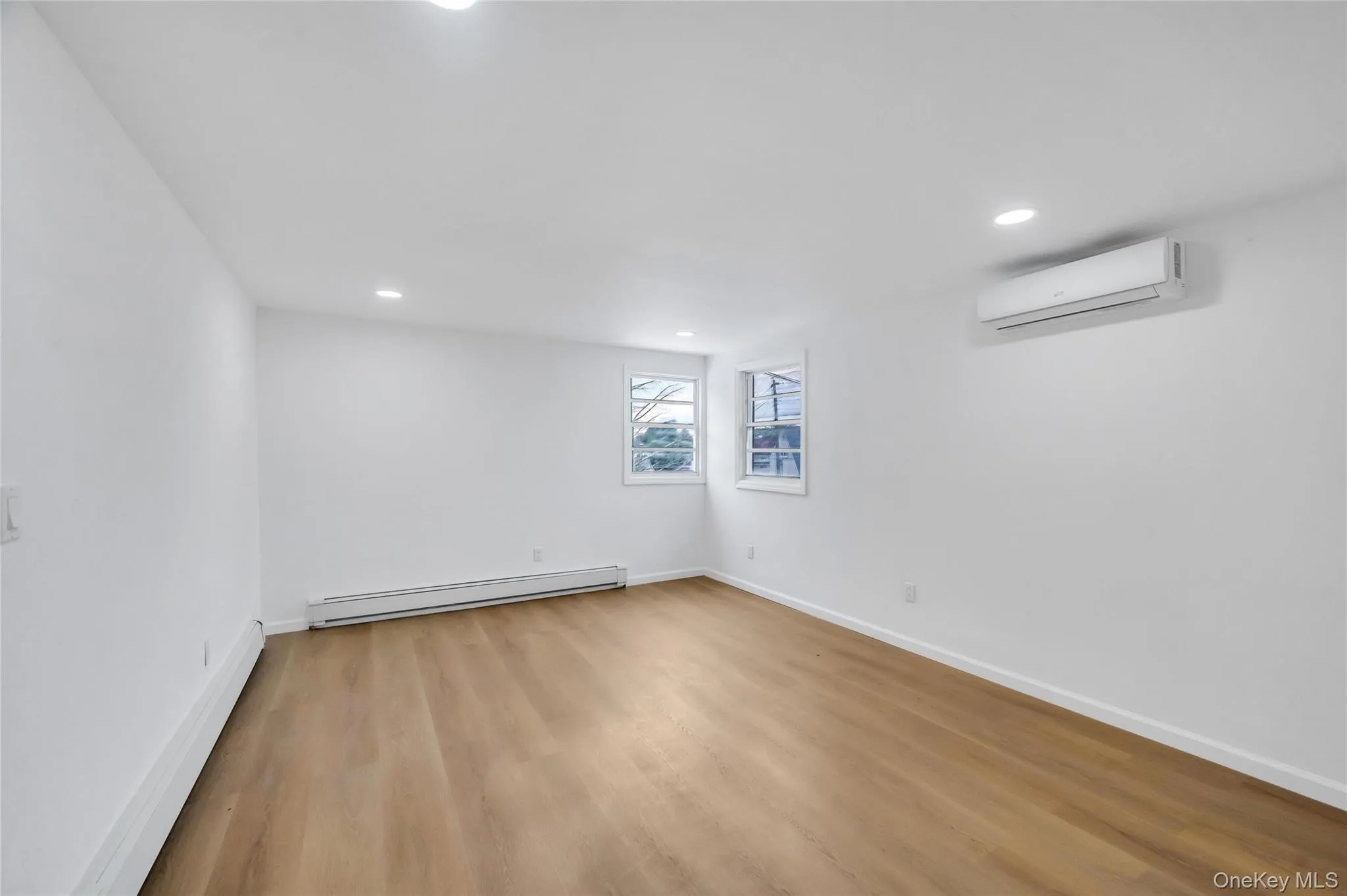 Spacious room featuring light wood-finish flooring, recessed lighting, white baseboards, and two windows Spacious room featuring light wood-finish flooring, recessed lighting, white baseboards, and two windows