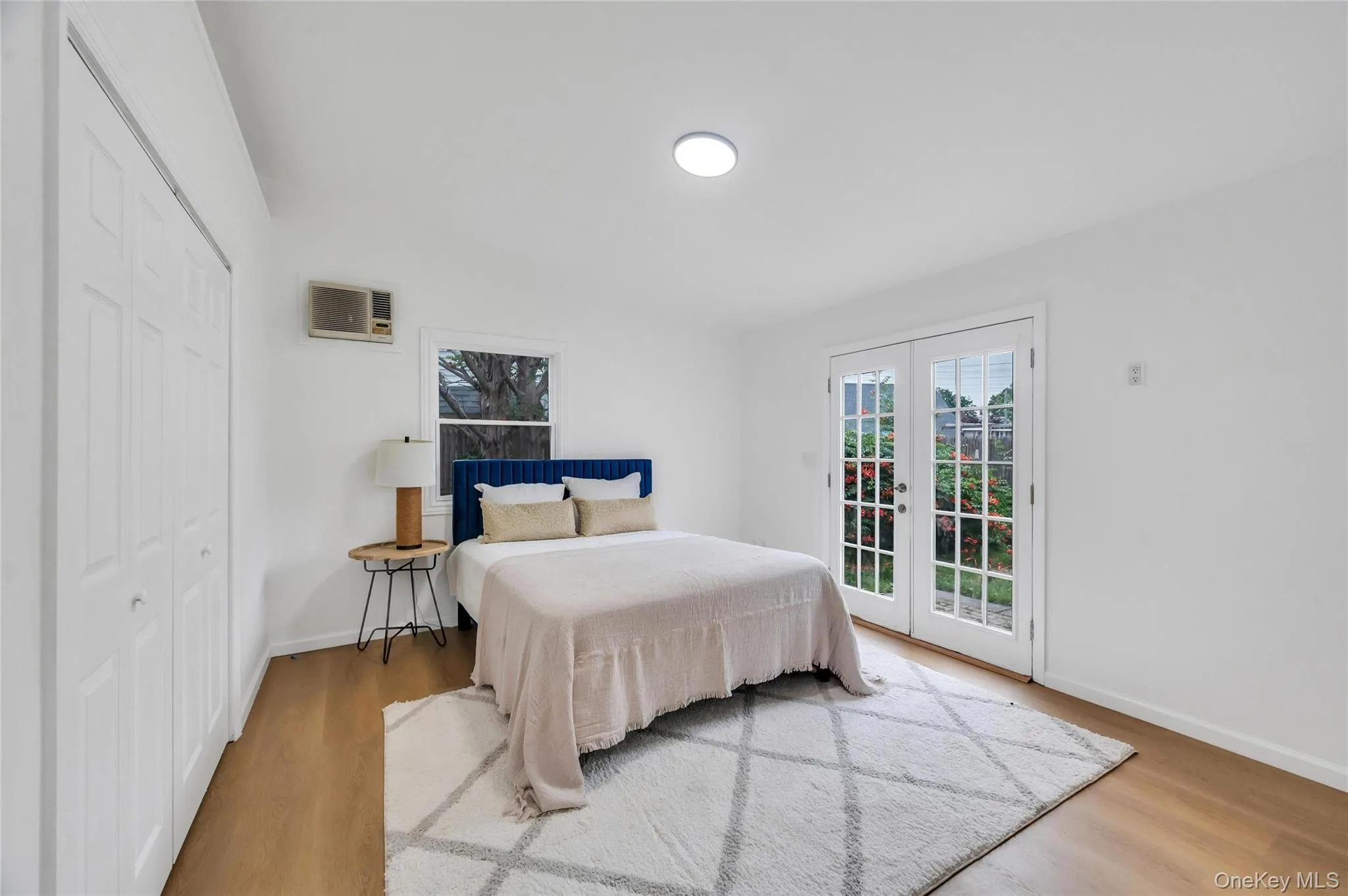 Bedroom featuring wood-finish flooring, white walls, and a ceiling-mounted light fixture Bedroom featuring wood-finish flooring, white walls, and a ceiling-mounted light fixture