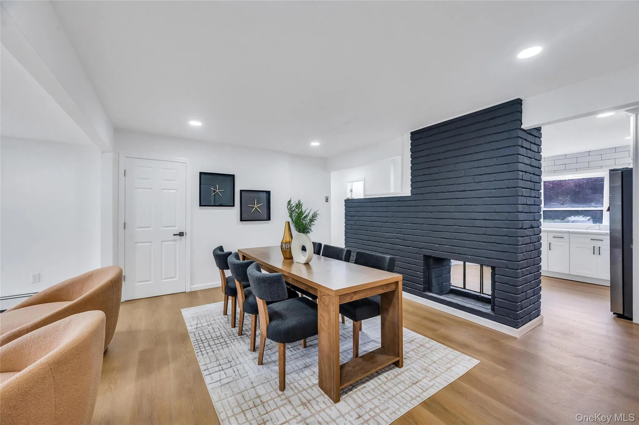 Open-concept living space featuring a black brick accent wall with an integrated fireplace, wood-finish flooring, and recessed lighting Open-concept living space featuring a black brick accent wall with an integrated fireplace, wood-finish flooring, and recessed lighting