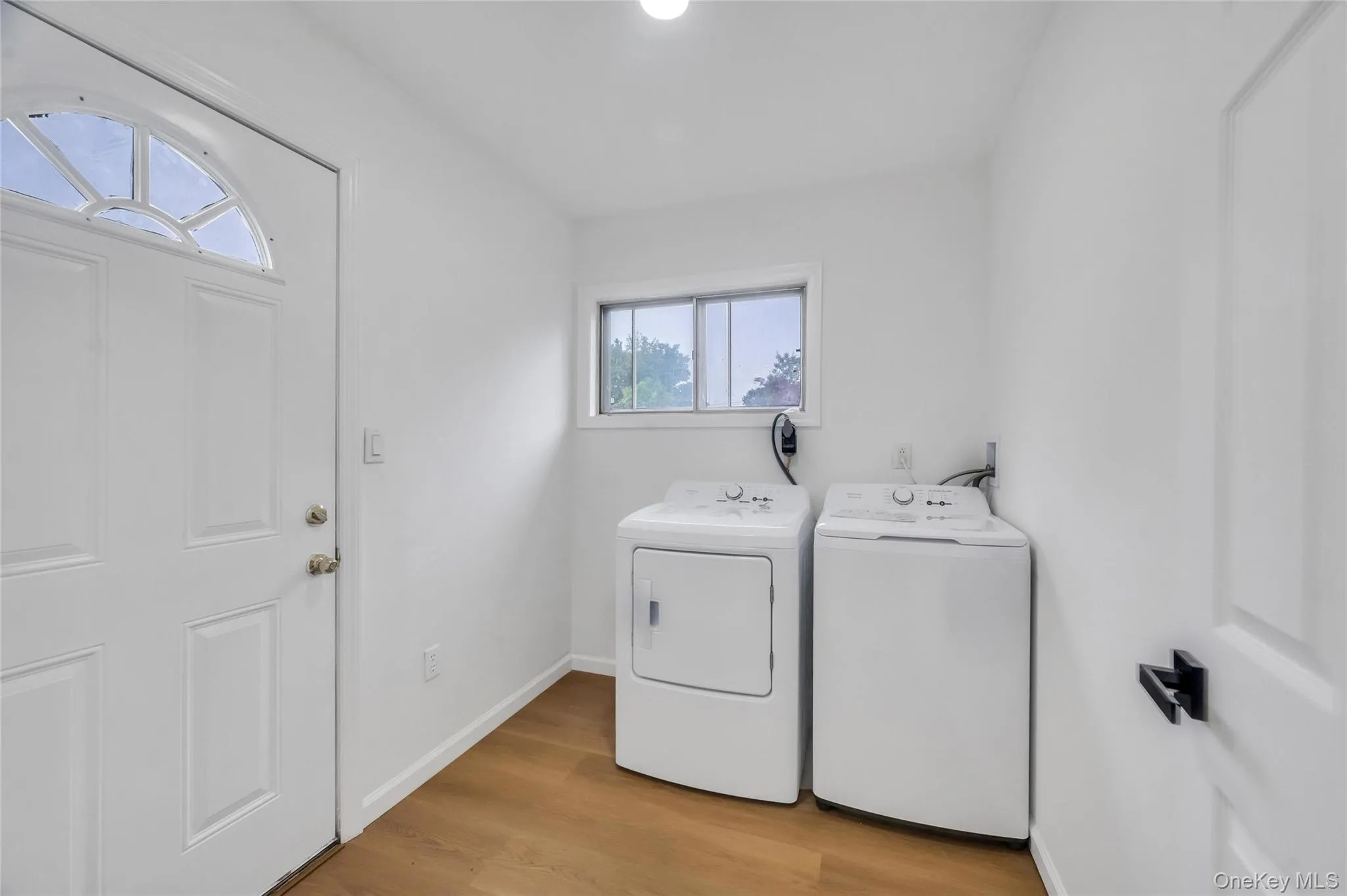 Dedicated laundry area featuring a window, wood-finish flooring, white walls, and a separate side door with a decorative glass insert Dedicated laundry area featuring a window, wood-finish flooring, white walls, and a separate side door with a decorative glass insert