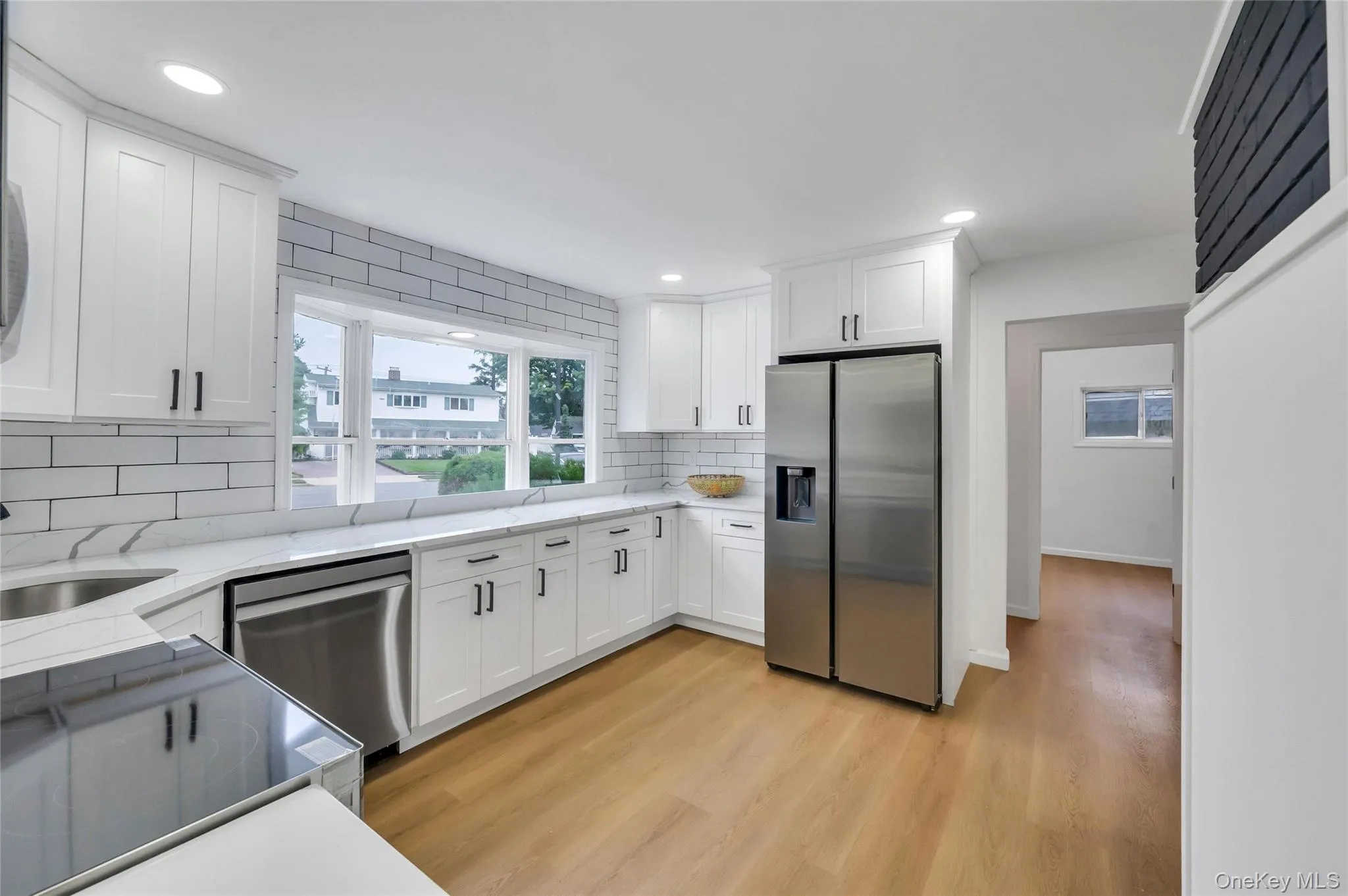 Kitchen featuring white shaker cabinetry, stainless steel appliances, white subway tile backsplash, light wood-finish flooring, and recessed lighting Kitchen featuring white shaker cabinetry, stainless steel appliances, white subway tile backsplash, light wood-finish flooring, and recessed lighting
