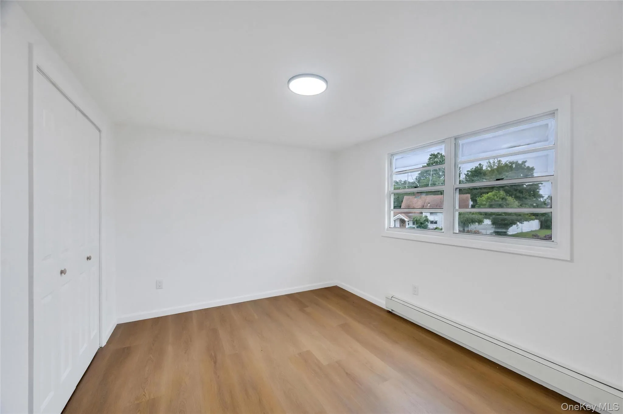Room featuring wood-finish flooring, white walls, and a multi-pane window Room featuring wood-finish flooring, white walls, and a multi-pane window