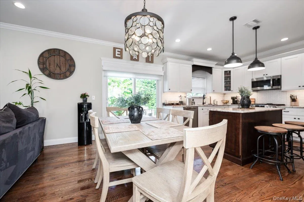 Open-concept kitchen and dining area featuring rich wood-finish flooring, white shaker cabinetry, stainless steel appliances, and a central island with a contrasting dark wood base Open-concept kitchen and dining area featuring rich wood-finish flooring, white shaker cabinetry, stainless steel appliances, and a central island with a contrasting dark wood base