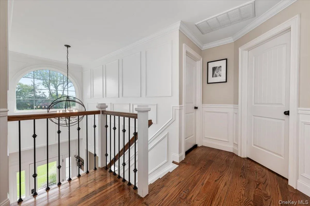 Upper landing featuring hardwood flooring, wainscoting, and an arched window Upper landing featuring hardwood flooring, wainscoting, and an arched window