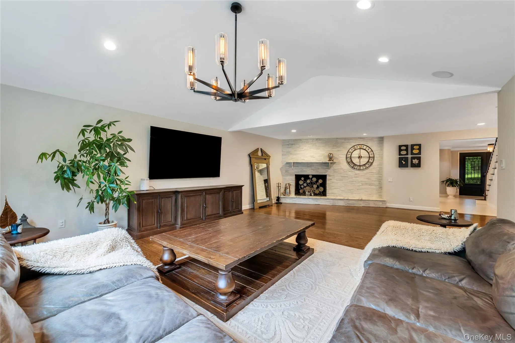 Living area featuring vaulted ceiling, wood finished floors, a large fireplace, a chandelier, and recessed lighting Living area featuring vaulted ceiling, wood finished floors, a large fireplace, a chandelier, and recessed lighting