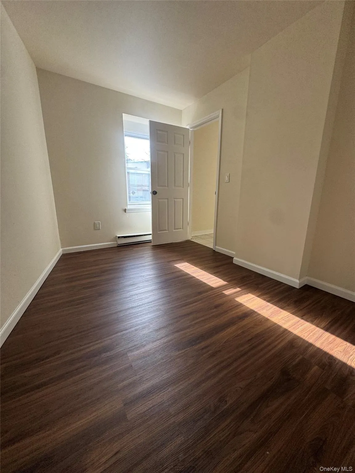 Empty room featuring dark wood-style floors and baseboard heating Empty room featuring dark wood-style floors and baseboard heating