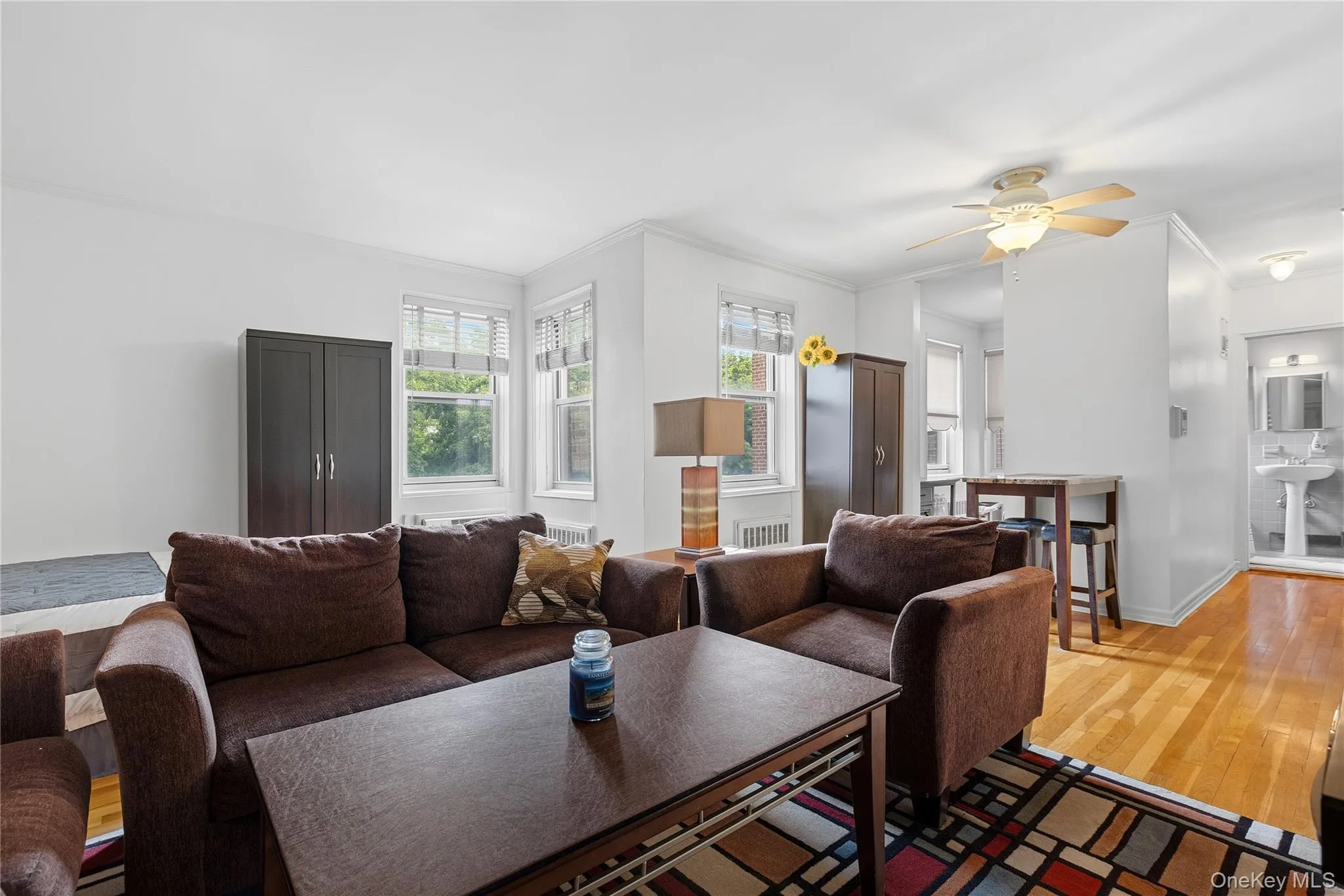Living area featuring hardwood flooring, multiple windows, a ceiling fan with light fixture, and white wall finishes Living area featuring hardwood flooring, multiple windows, a ceiling fan with light fixture, and white wall finishes