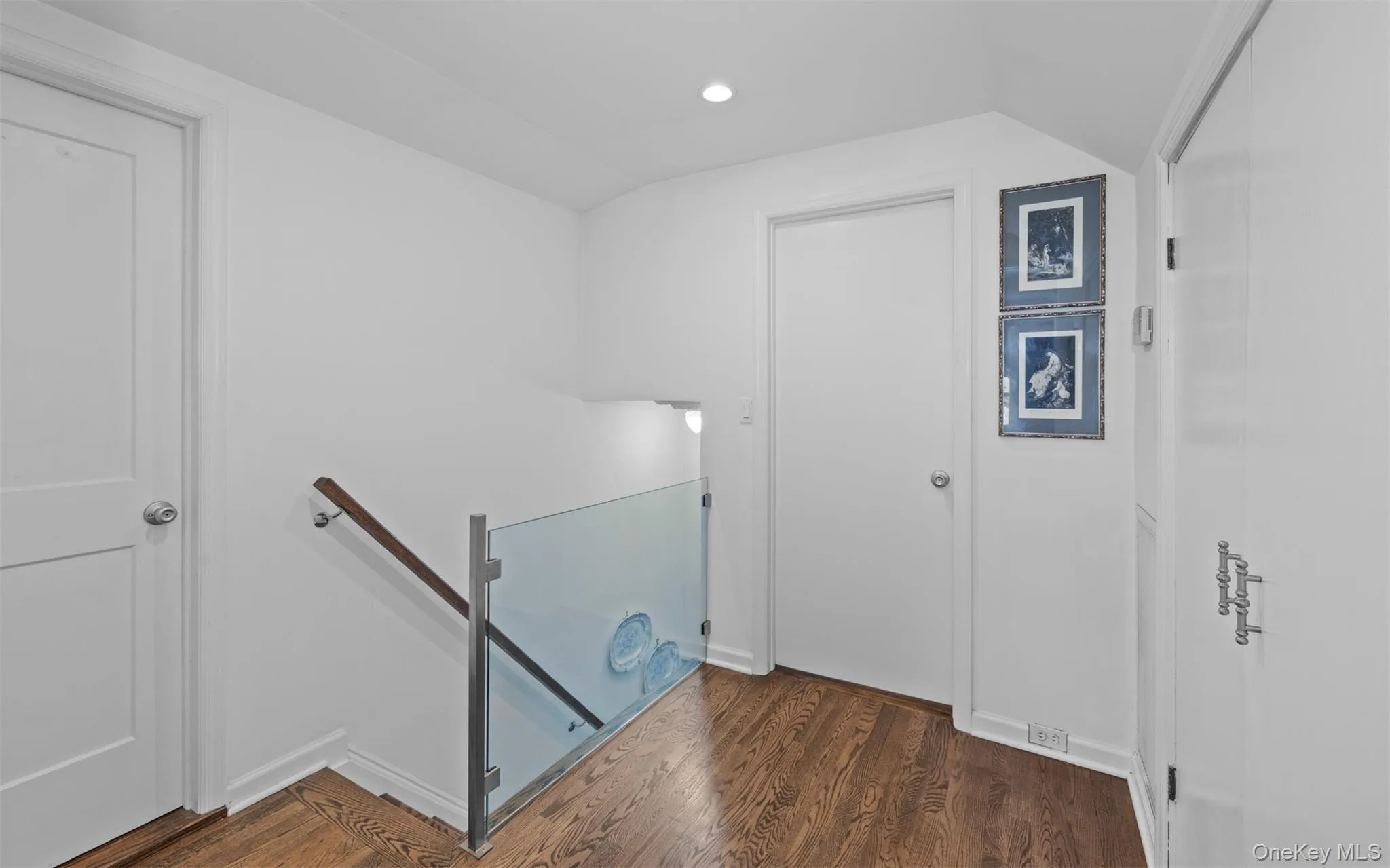 Second floor landing featuring glass banister and hardwood flooring Second floor landing featuring glass banister and hardwood flooring