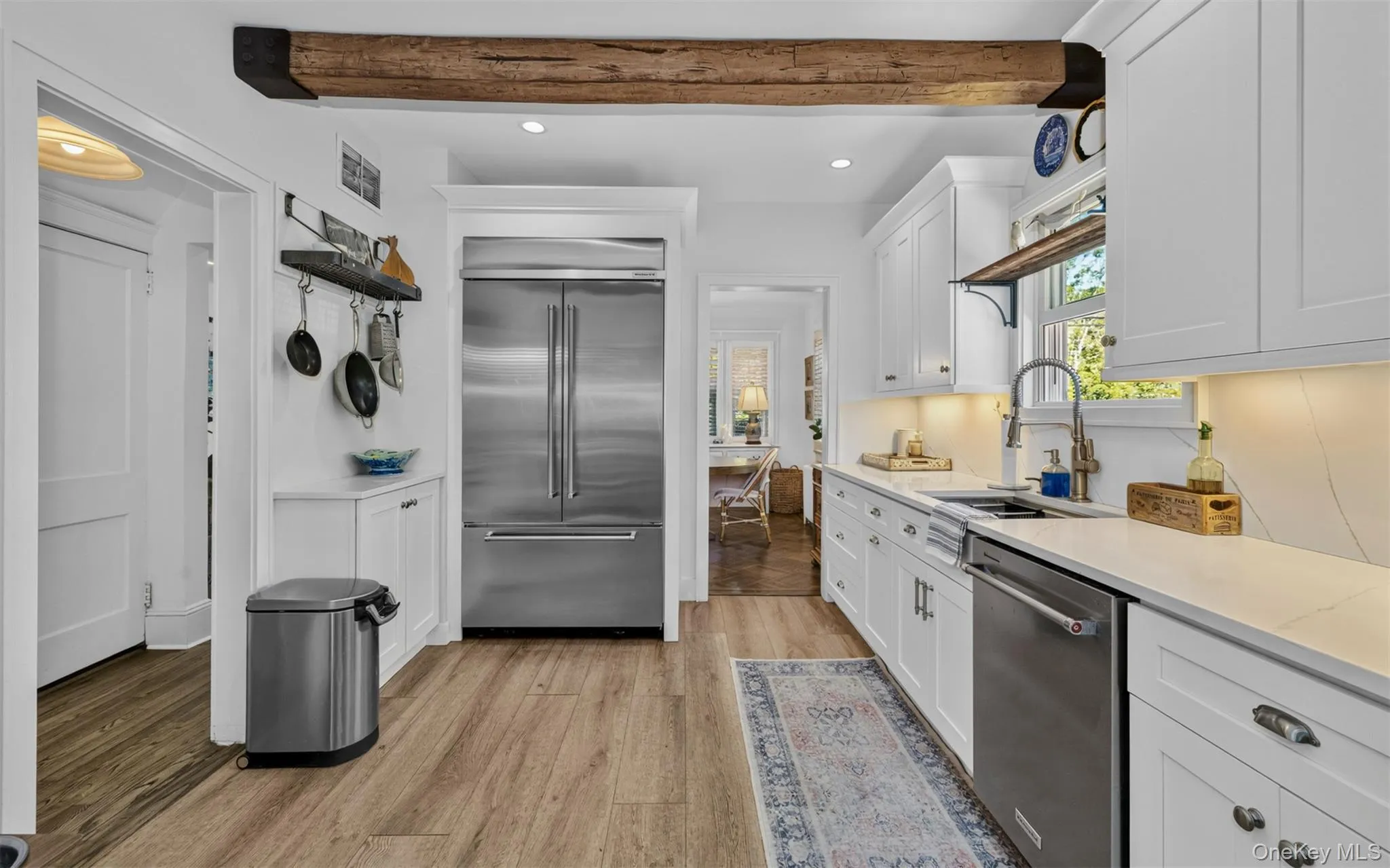Kitchen featuring a prominent wood beam, white shaker cabinetry, stainless steel appliances, light-toned countertops, and hardwood flooring Kitchen featuring a prominent wood beam, white shaker cabinetry, stainless steel appliances, light-toned countertops, and hardwood flooring