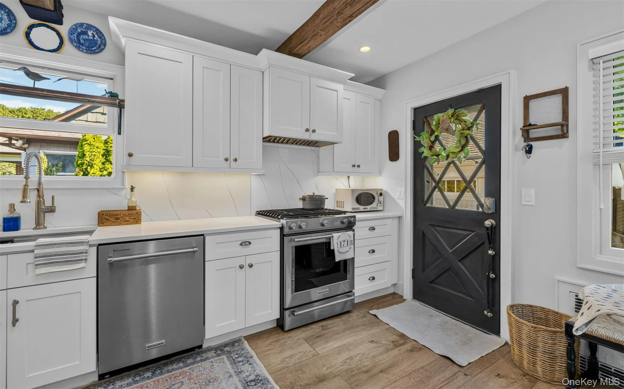 Kitchen featuring white cabinetry, stainless steel appliances, a farmhouse-style sink with a gooseneck faucet, light-colored countertops, and hardwood flooring Kitchen featuring white cabinetry, stainless steel appliances, a farmhouse-style sink with a gooseneck faucet, light-colored countertops, and hardwood flooring