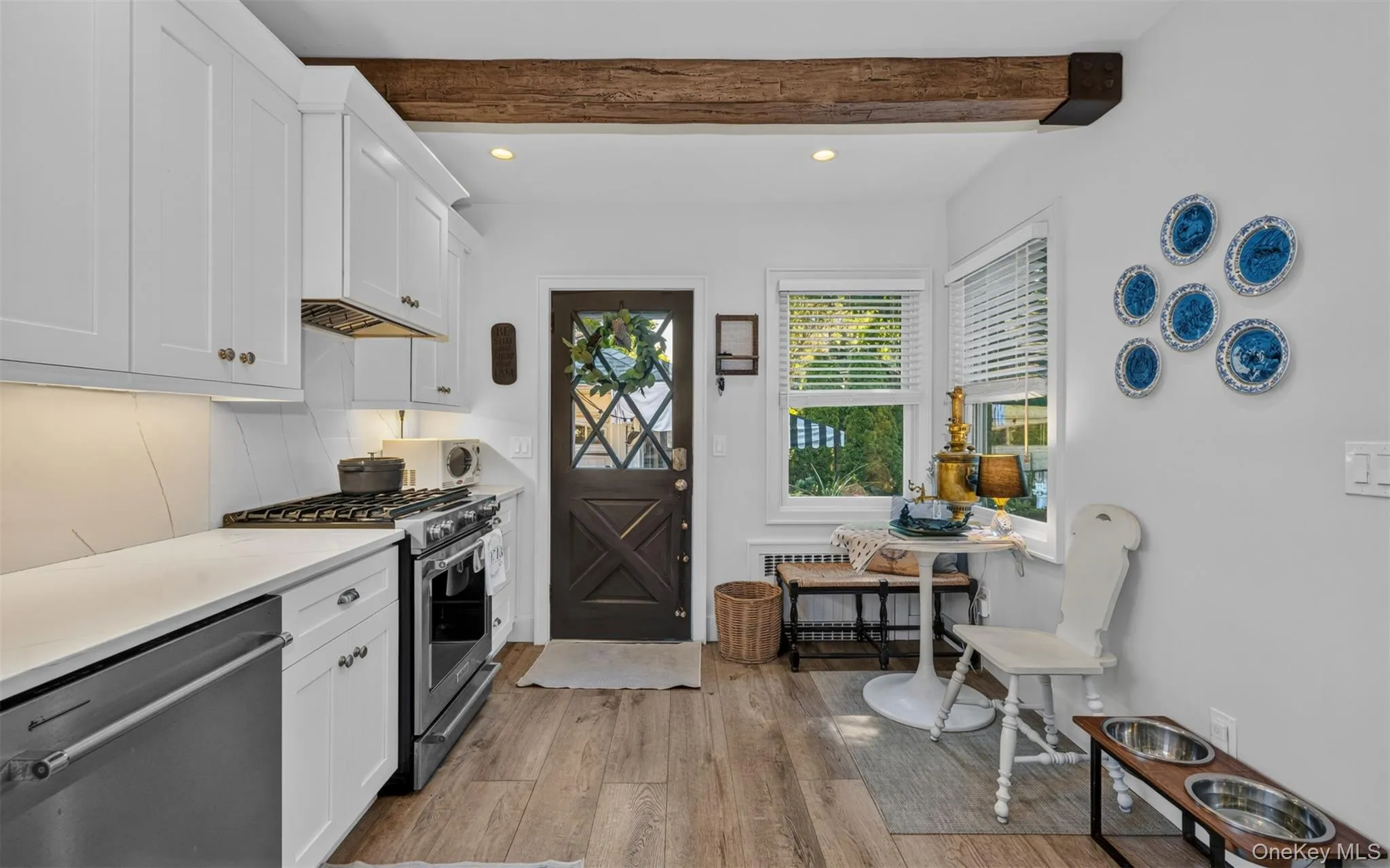 Kitchen featuring a prominent wood beam, white shaker cabinetry, stainless steel appliances, light-toned countertops, and hardwood flooring Kitchen featuring a prominent wood beam, white shaker cabinetry, stainless steel appliances, light-toned countertops, and hardwood flooring