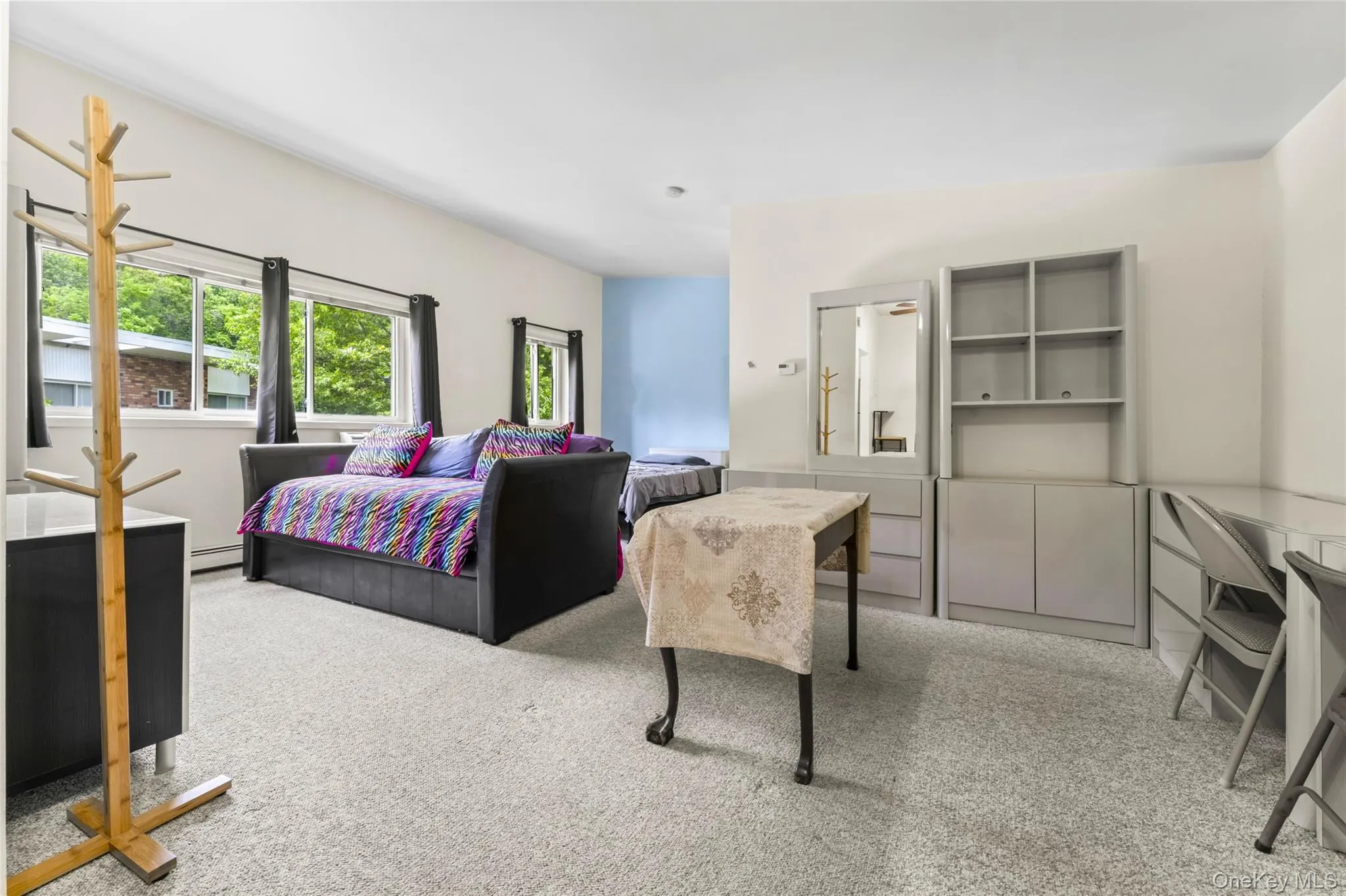 Carpeted living space with multiple windows, a light blue accent wall, and built-in shelving units Carpeted living space with multiple windows, a light blue accent wall, and built-in shelving units