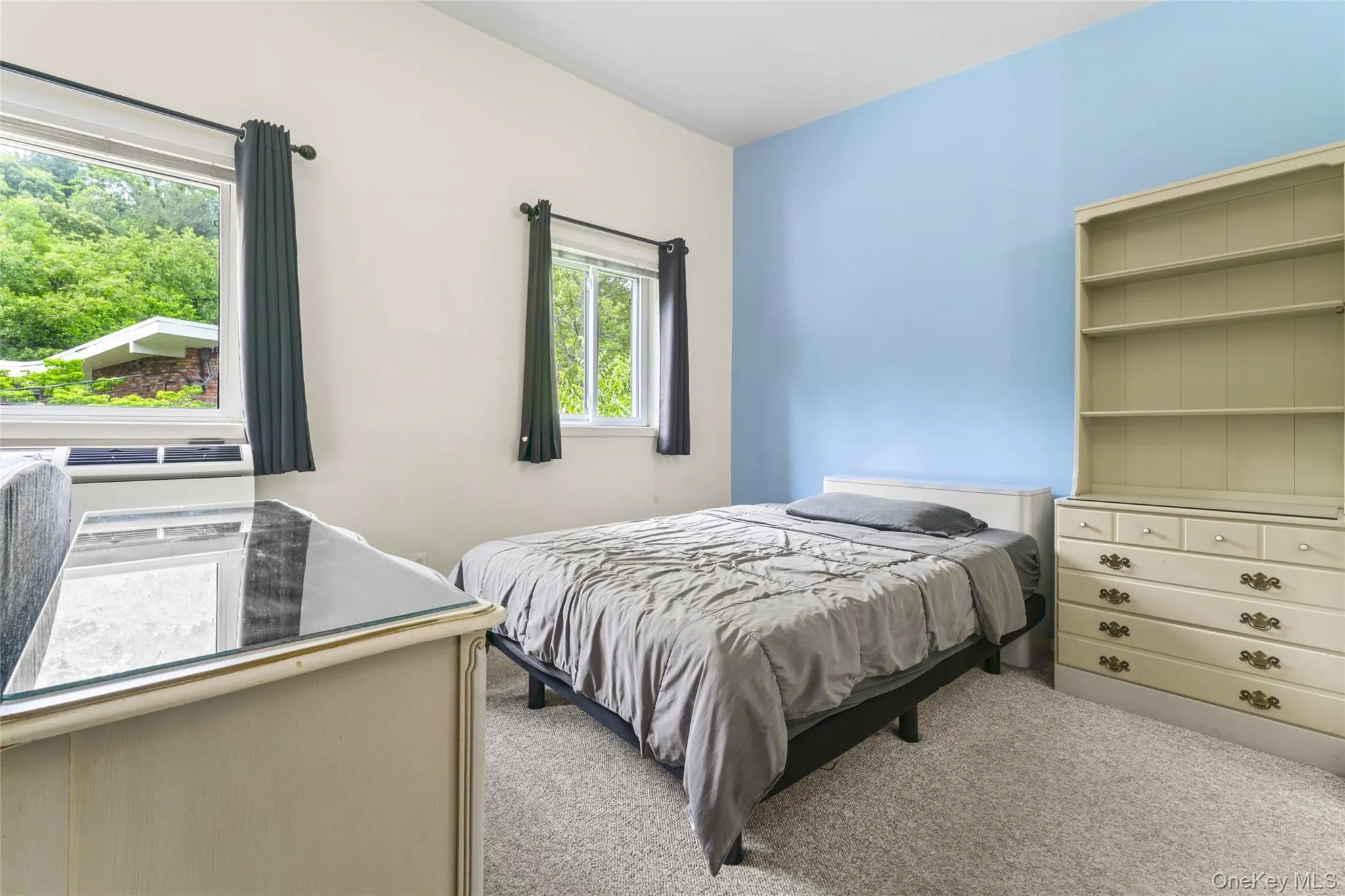 Carpeted interior with multiple windows, a light blue accent wall, and a built-in air conditioning unit Carpeted interior with multiple windows, a light blue accent wall, and a built-in air conditioning unit