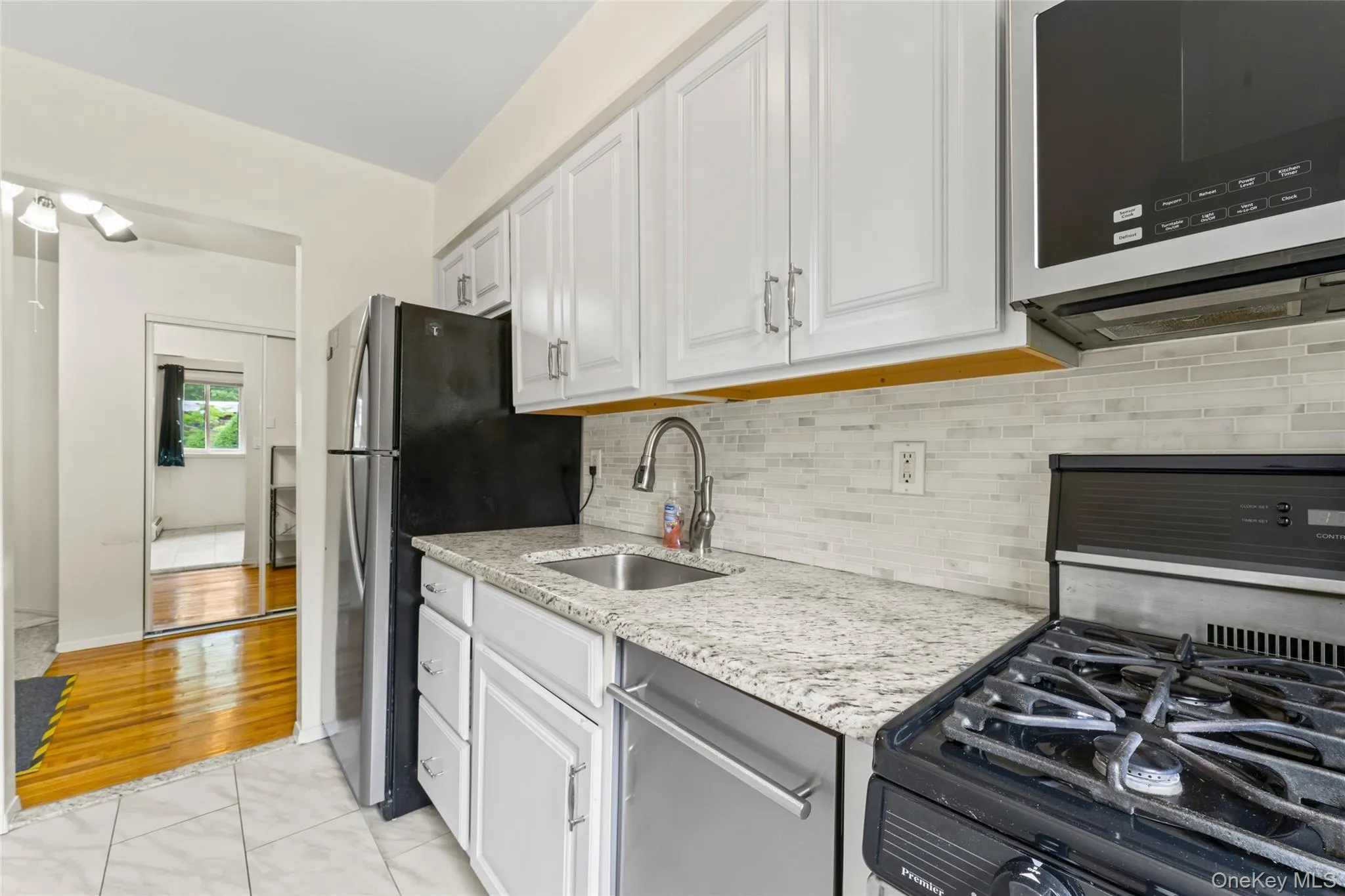 Kitchen featuring white cabinetry, light-toned granite-style countertops, stainless steel appliances, and a tiled backsplash Kitchen featuring white cabinetry, light-toned granite-style countertops, stainless steel appliances, and a tiled backsplash