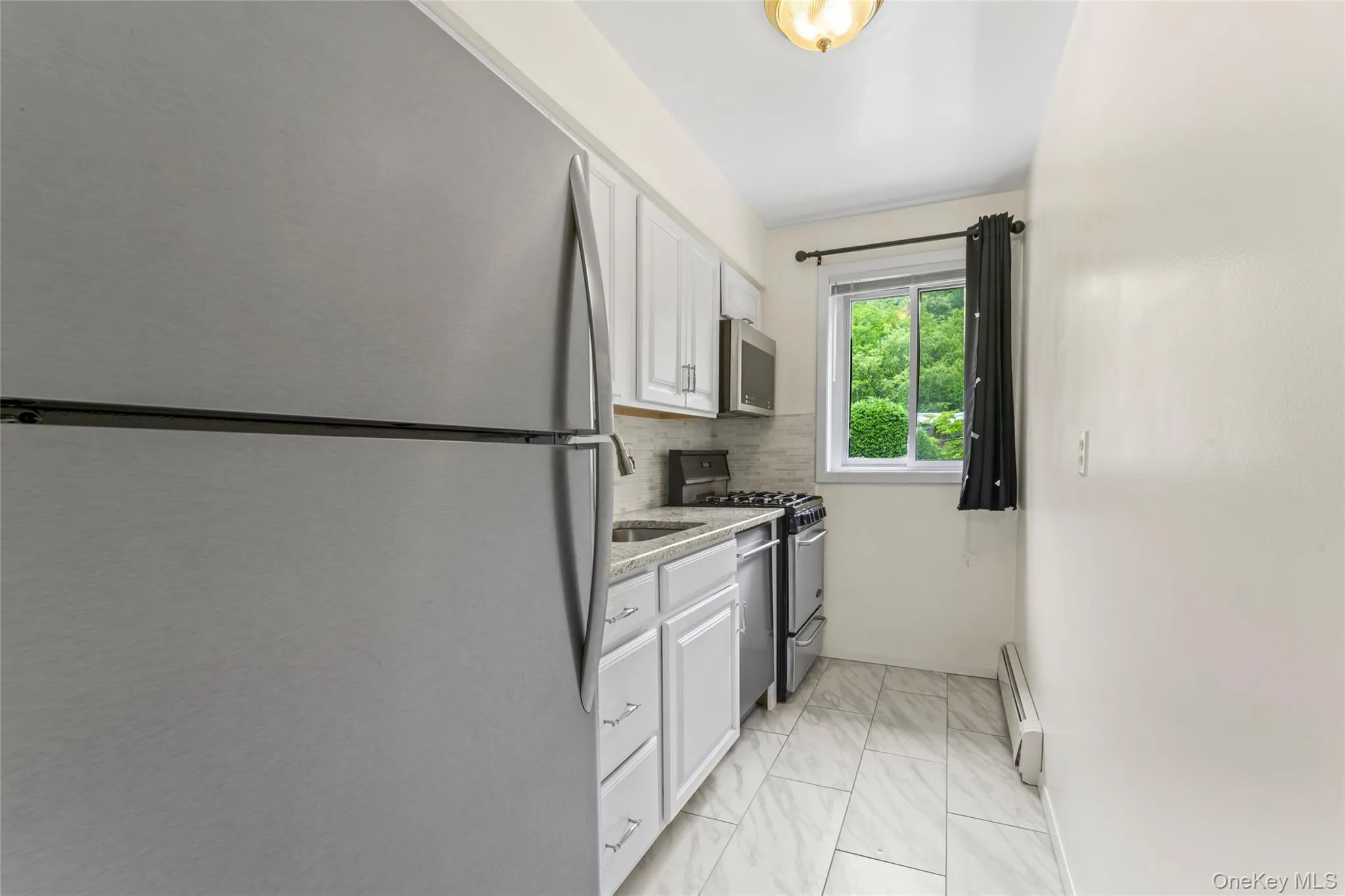 Streamlined kitchen featuring white cabinetry, light-toned countertops, and a full suite of stainless steel appliances Streamlined kitchen featuring white cabinetry, light-toned countertops, and a full suite of stainless steel appliances