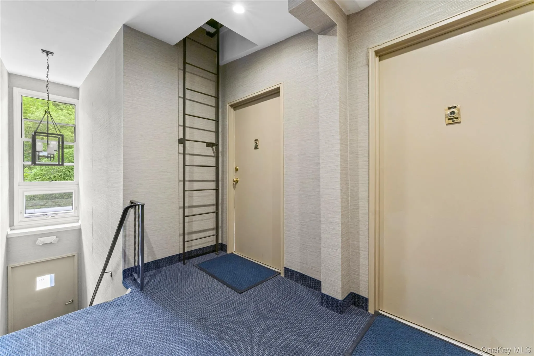 Entryway featuring a window with exterior greenery, a black metal hanging lantern, textured wall coverings, and a blue patterned carpet Entryway featuring a window with exterior greenery, a black metal hanging lantern, textured wall coverings, and a blue patterned carpet