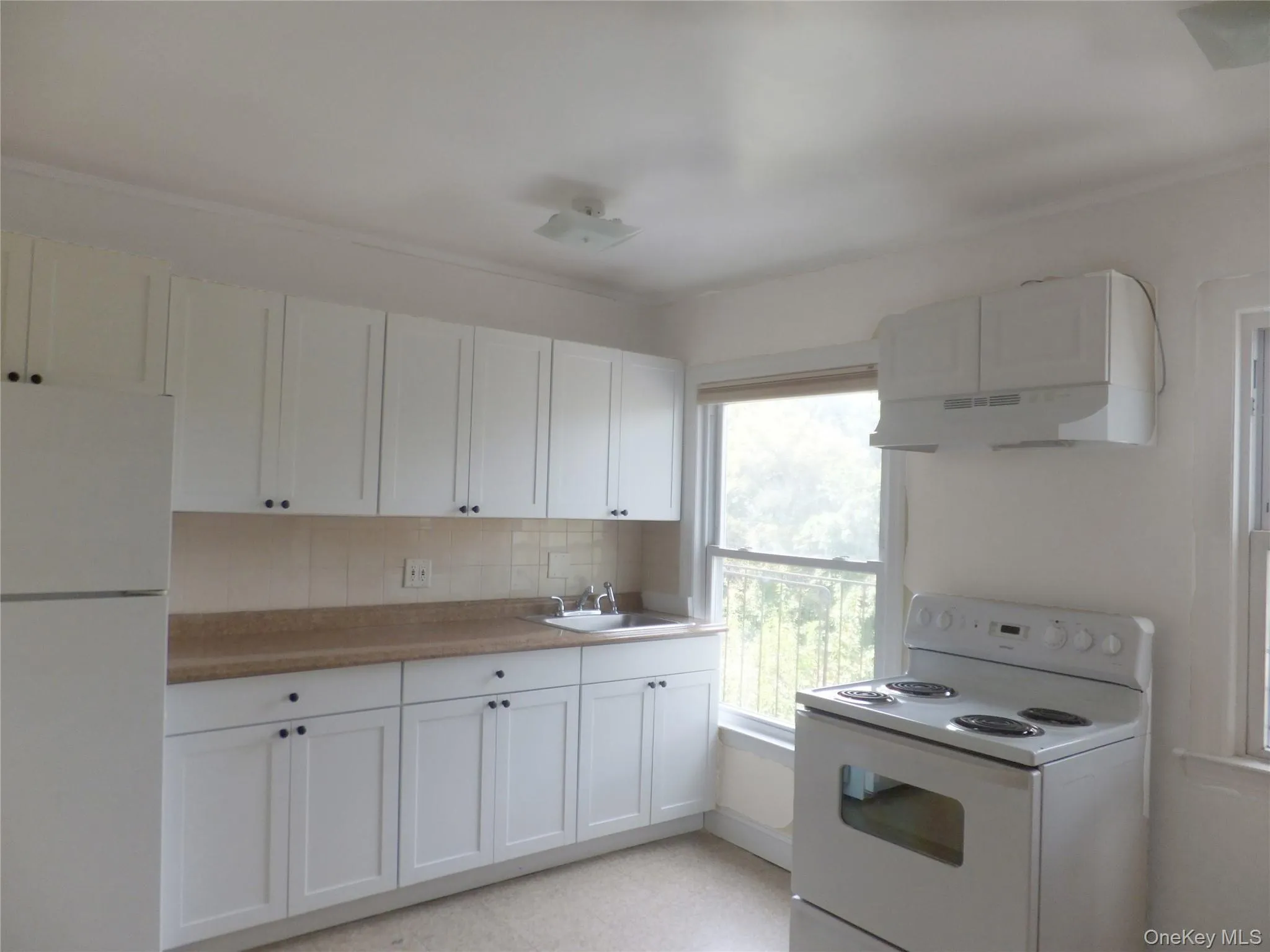 Kitchen with white appliances, light countertops, white cabinets, under cabinet range hood, and tasteful backsplash Kitchen with white appliances, light countertops, white cabinets, under cabinet range hood, and tasteful backsplash