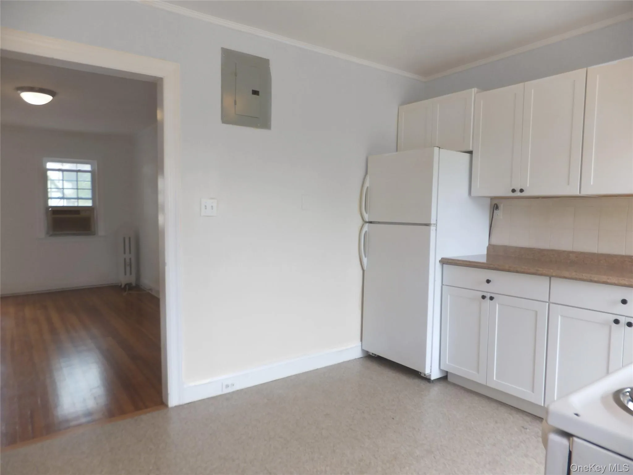 Kitchen featuring white appliances, white cabinets, electric panel, ornamental molding, and tasteful backsplash Kitchen featuring white appliances, white cabinets, electric panel, ornamental molding, and tasteful backsplash