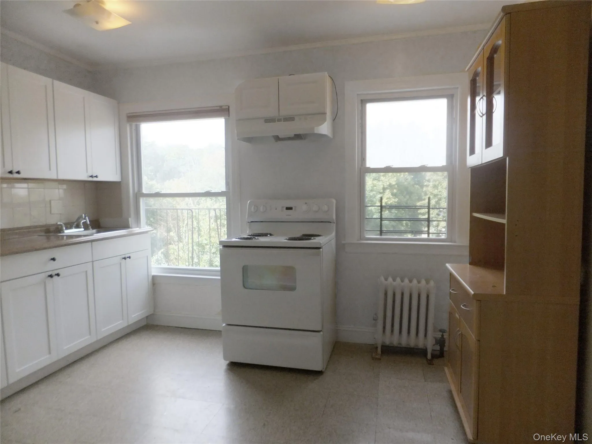 Kitchen with white range with electric stovetop, light floors, radiator, under cabinet range hood, and crown molding Kitchen with white range with electric stovetop, light floors, radiator, under cabinet range hood, and crown molding